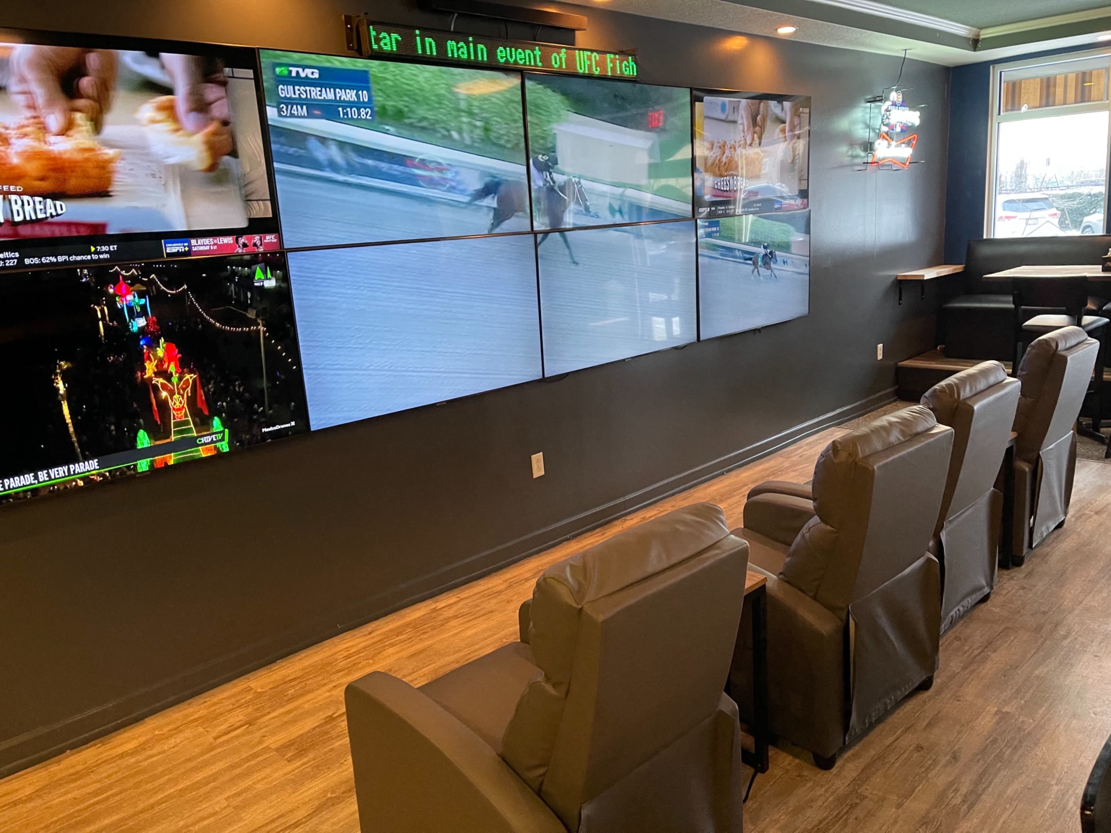 A seating area with multiple large screens displaying various sports events on a dark wall.