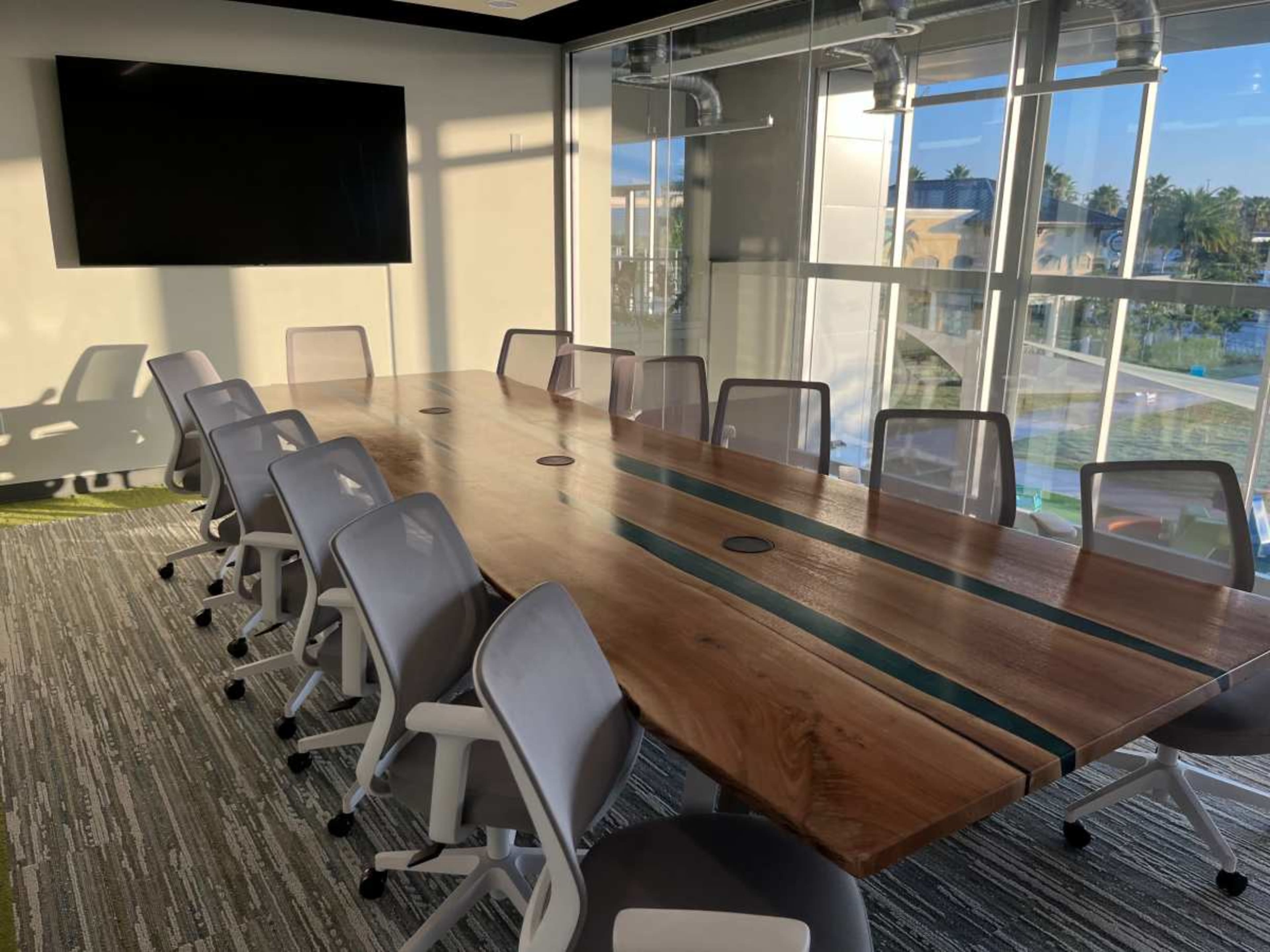 A long wooden conference table with built-in outlets is surrounded by modern chairs in a brightly lit meeting room.