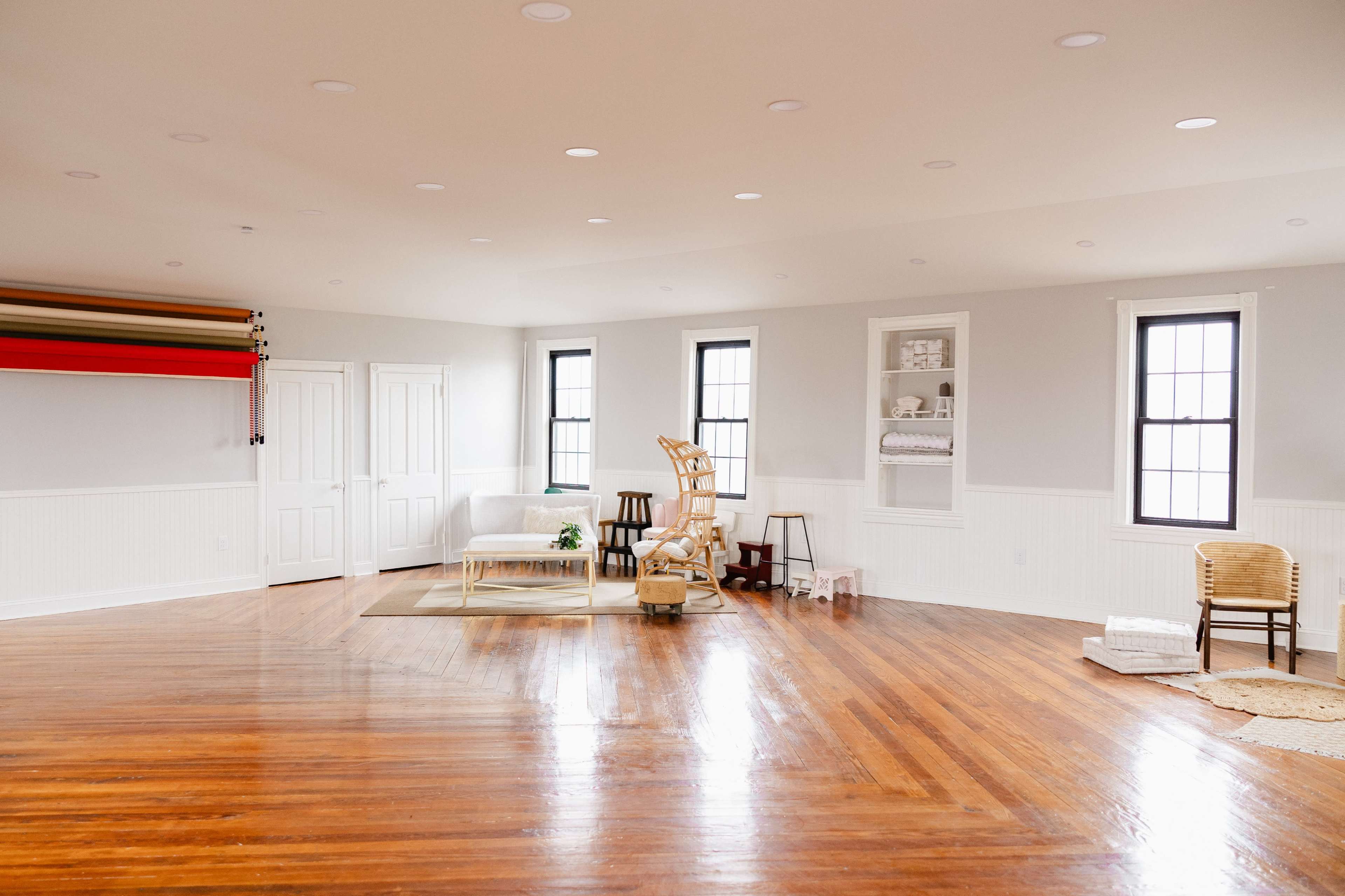 A spacious room with hardwood floors, large windows, and a cozy seating area featuring a white couch and a chair.