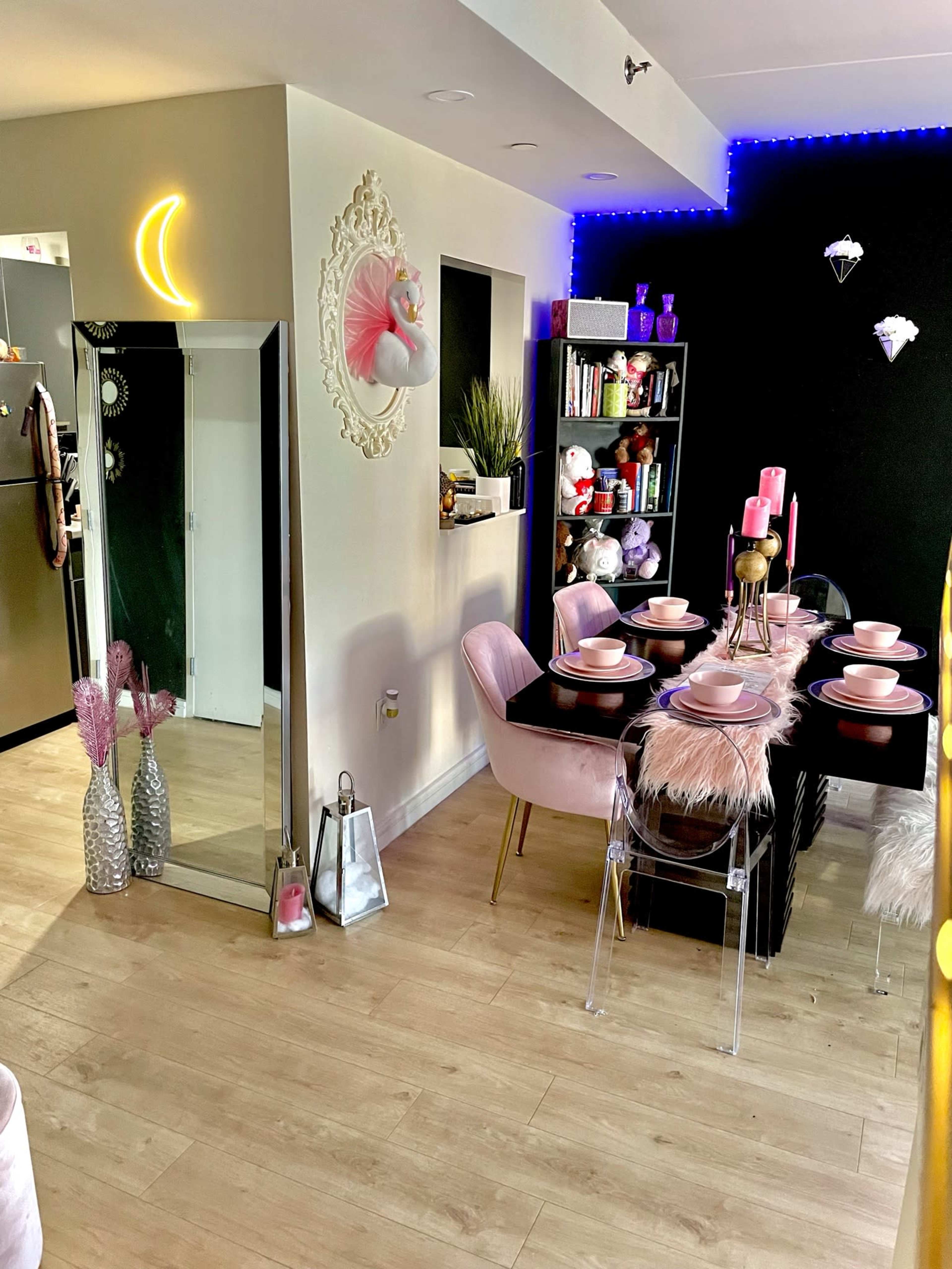 A modern dining area featuring a table set with pink dishware, surrounded by stylish chairs, and decorated with colorful lighting and various decor items.