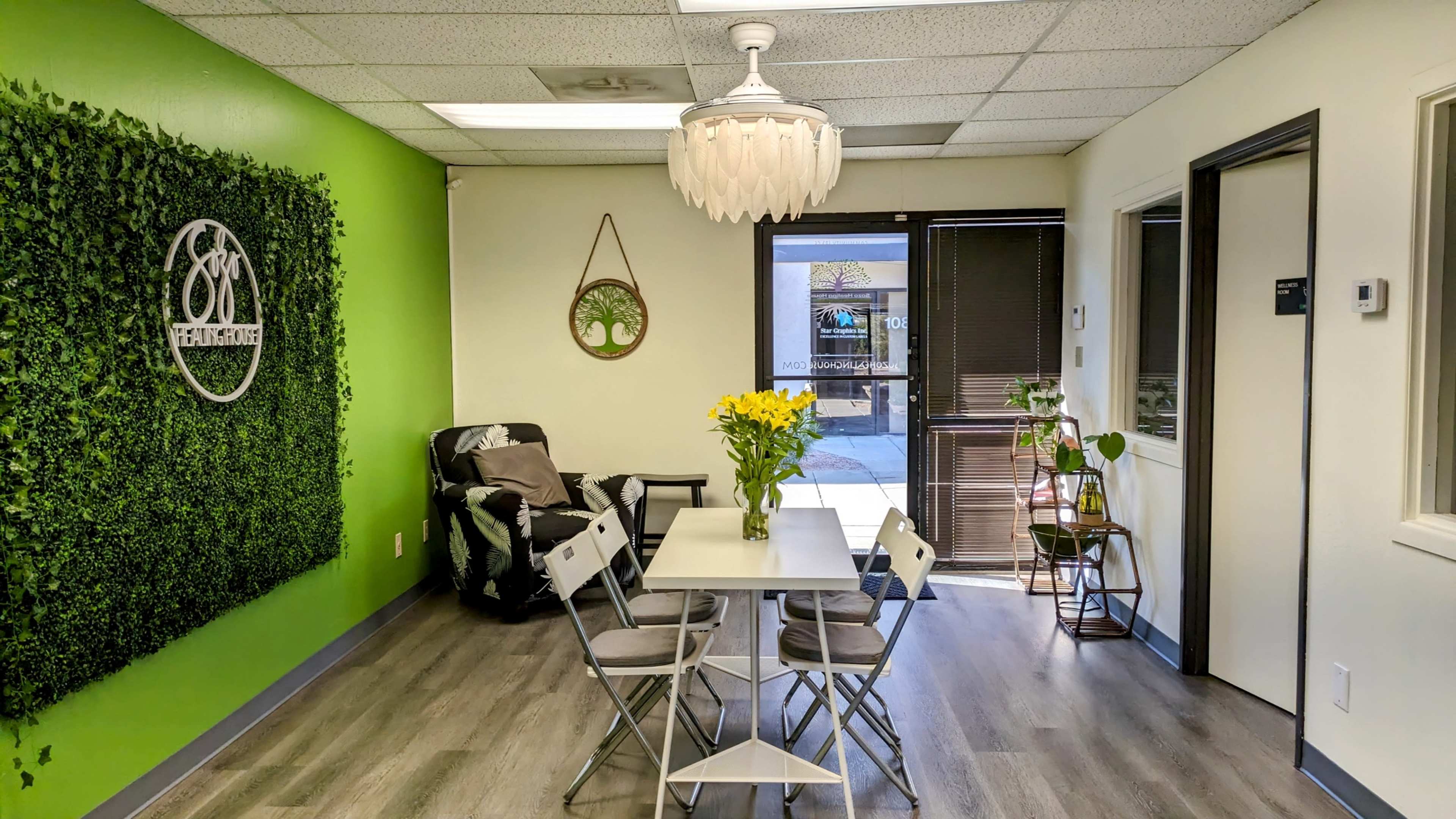 A contemporary waiting area with a green accent wall, a seating area with a plant, and a white table set with chairs.