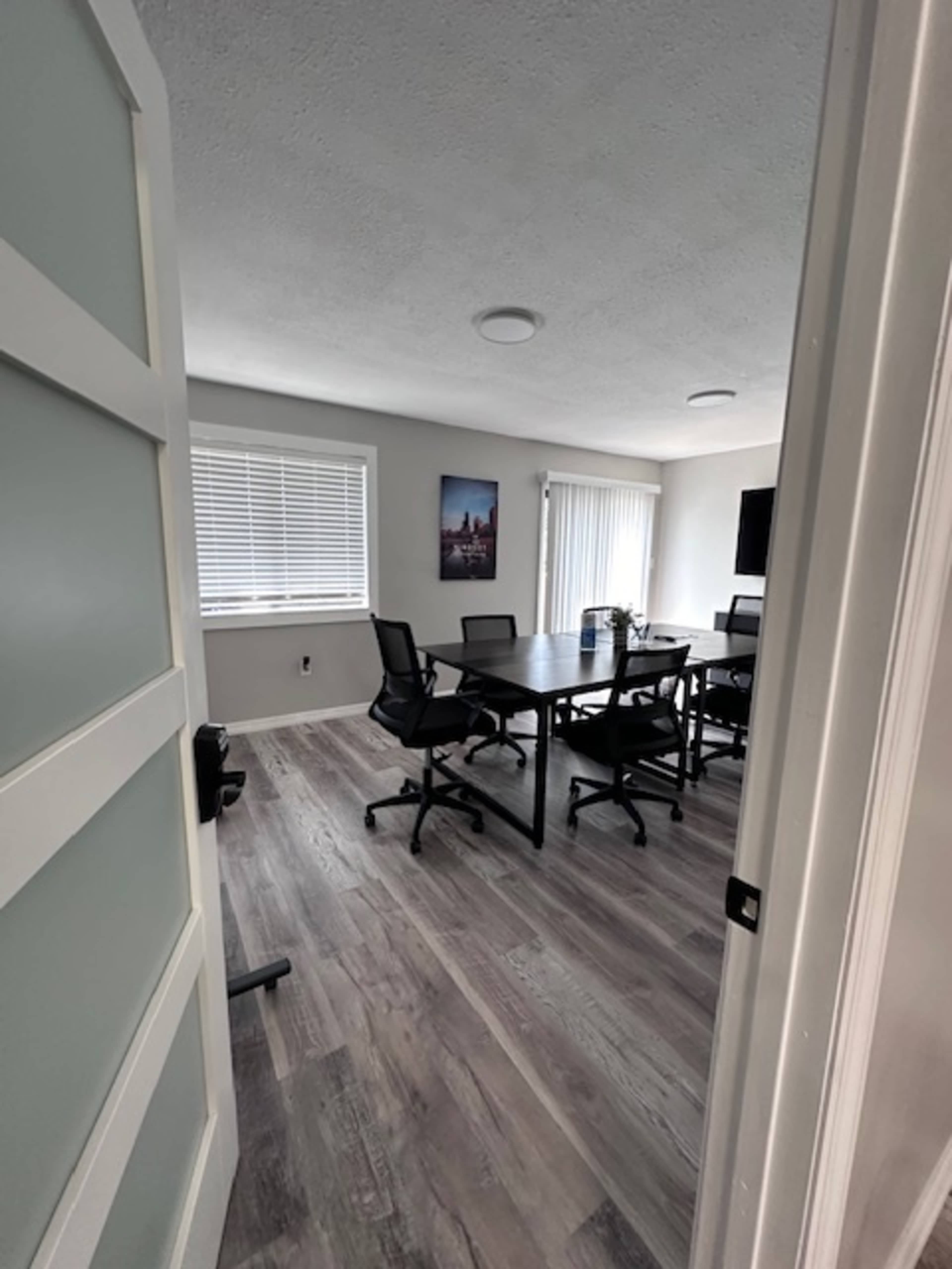 A modern conference room with a large table, several black chairs, and a wall adorned with a framed cityscape photo.