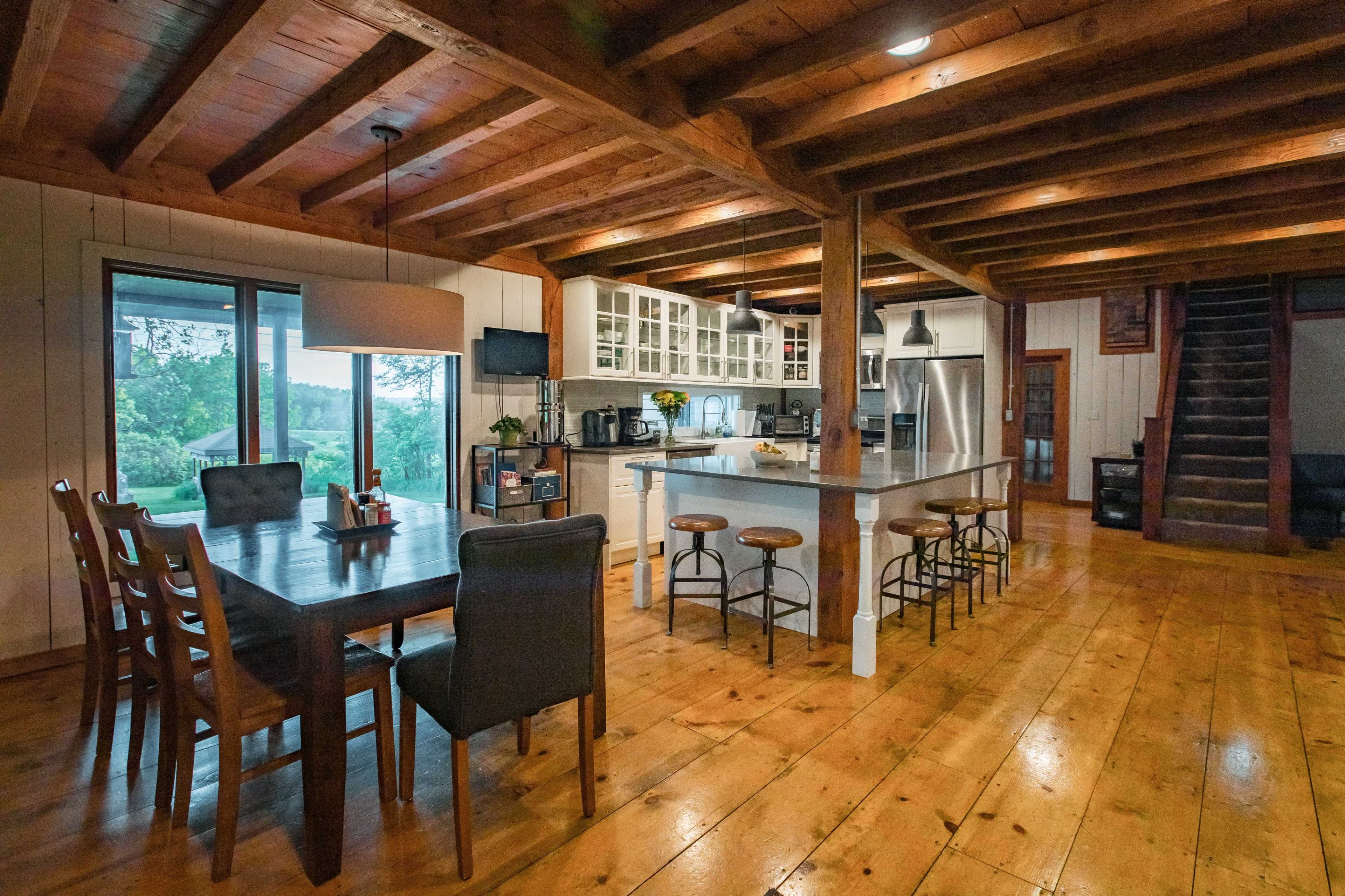 A spacious kitchen and dining area with wooden beams, a large table, and a modern kitchen equipped with stainless steel appliances.