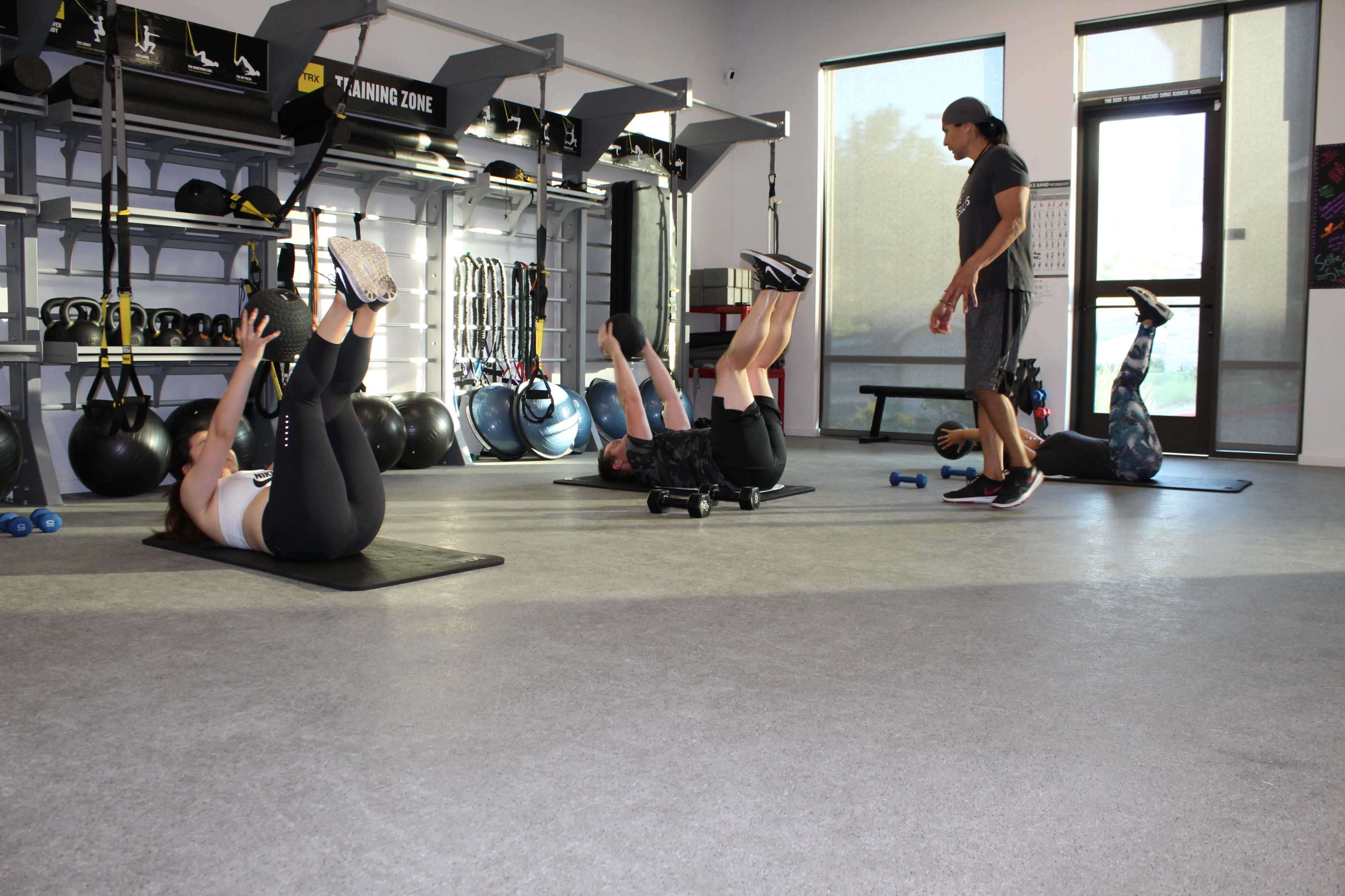 A fitness studio features four individuals engaged in core exercises with equipment like dumbbells and mats.
