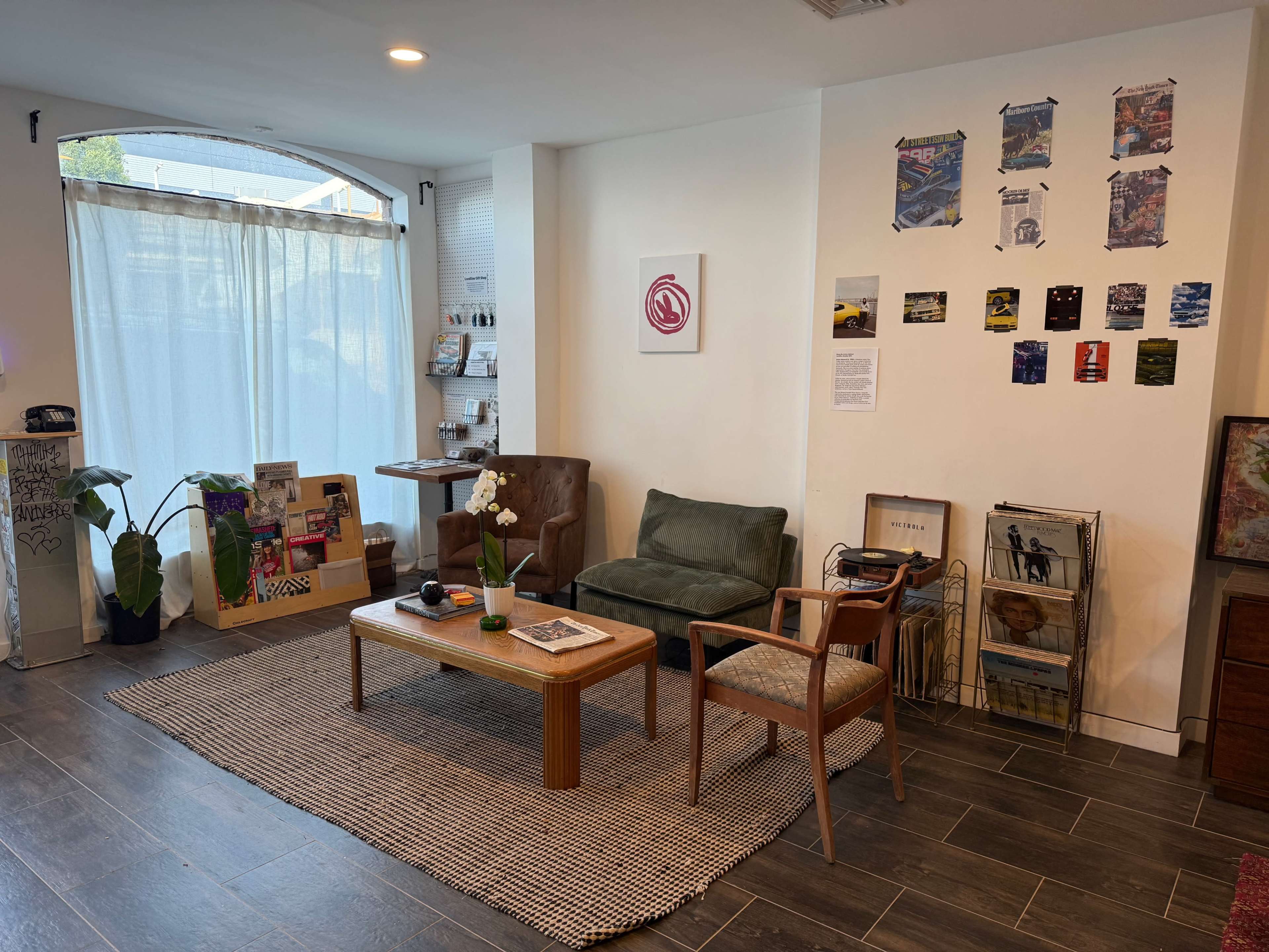 The image shows a cozy reception area with two chairs, a coffee table, a plant, and various wall decorations, including framed posters and informational displays.