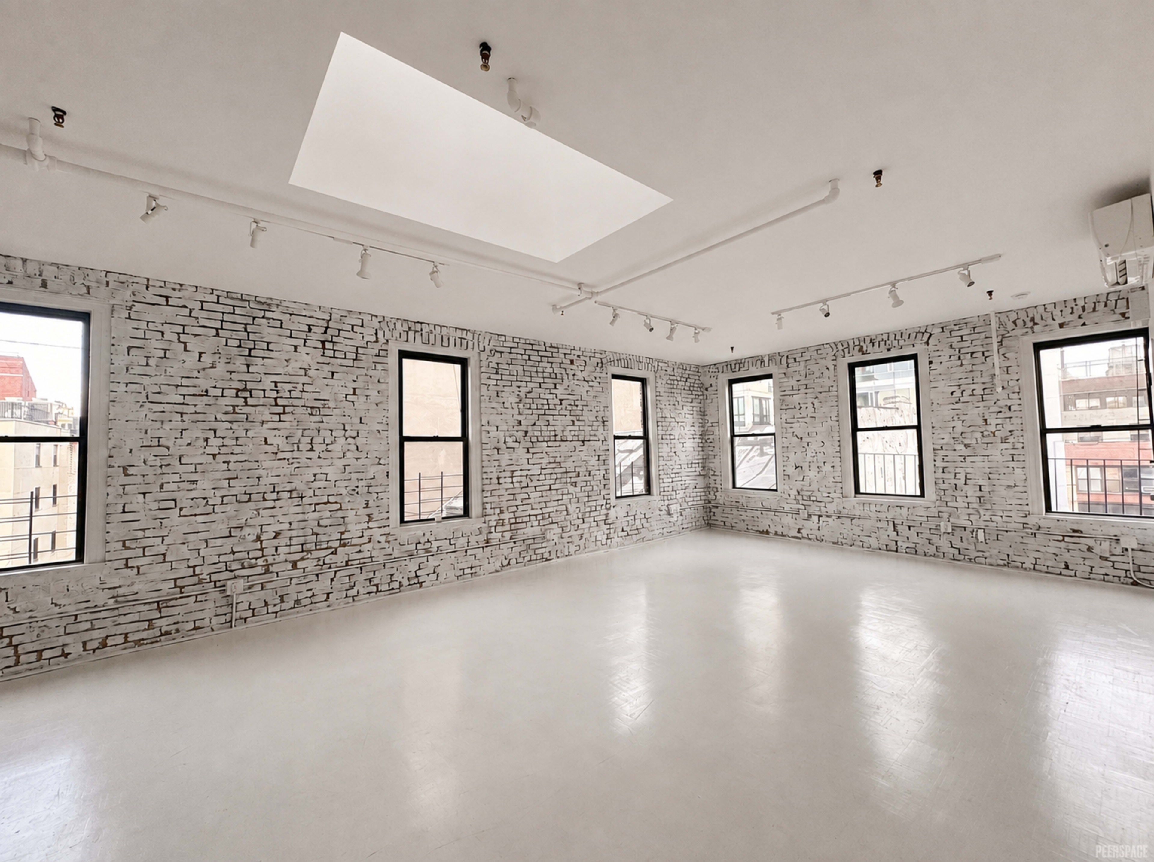 The image shows a spacious, modern room with white brick walls, large windows, and a skylight providing natural light.