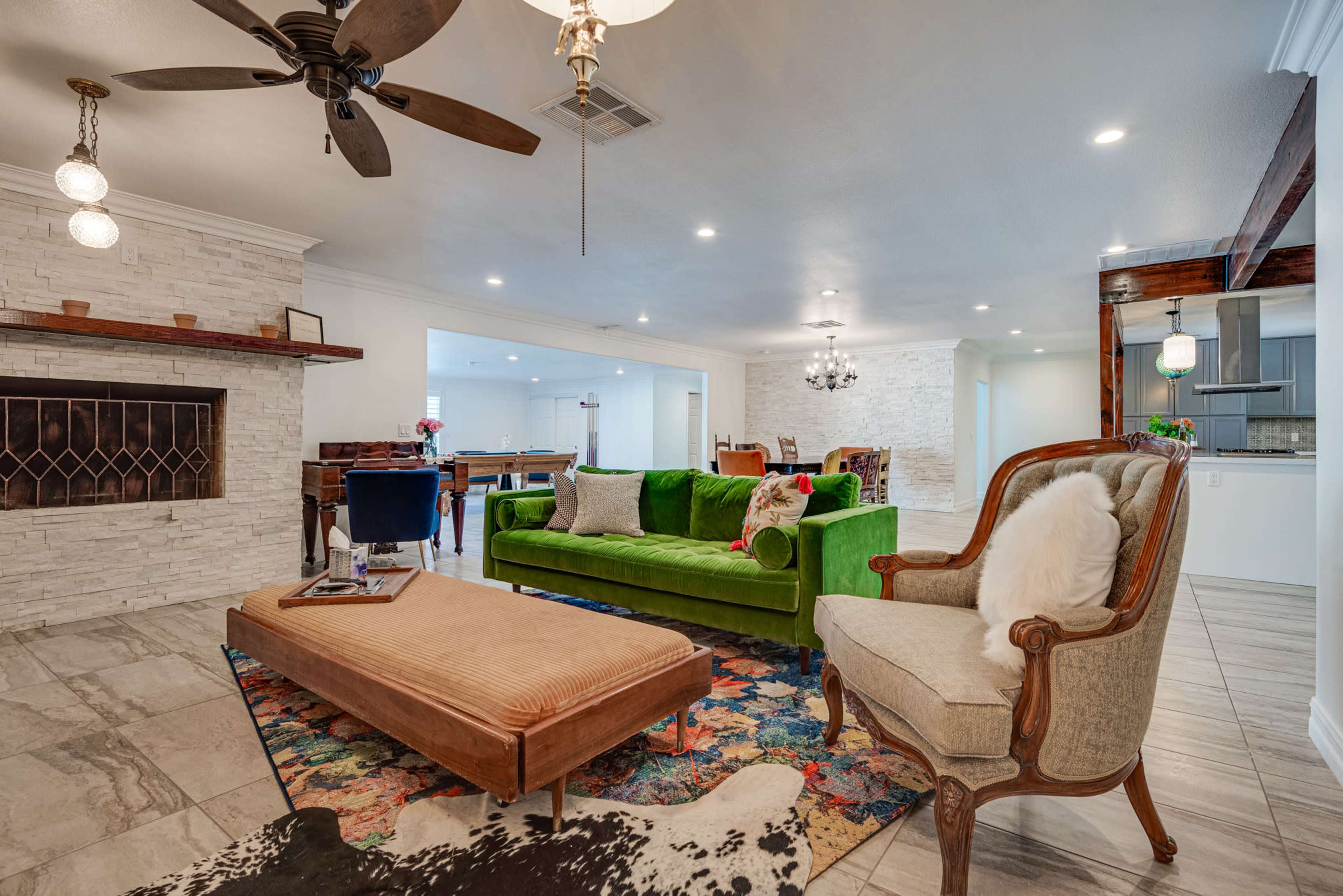 A bright living room featuring a green couch, a patterned rug, and a decorative coffee table, with a fireplace and an open layout leading to another space.