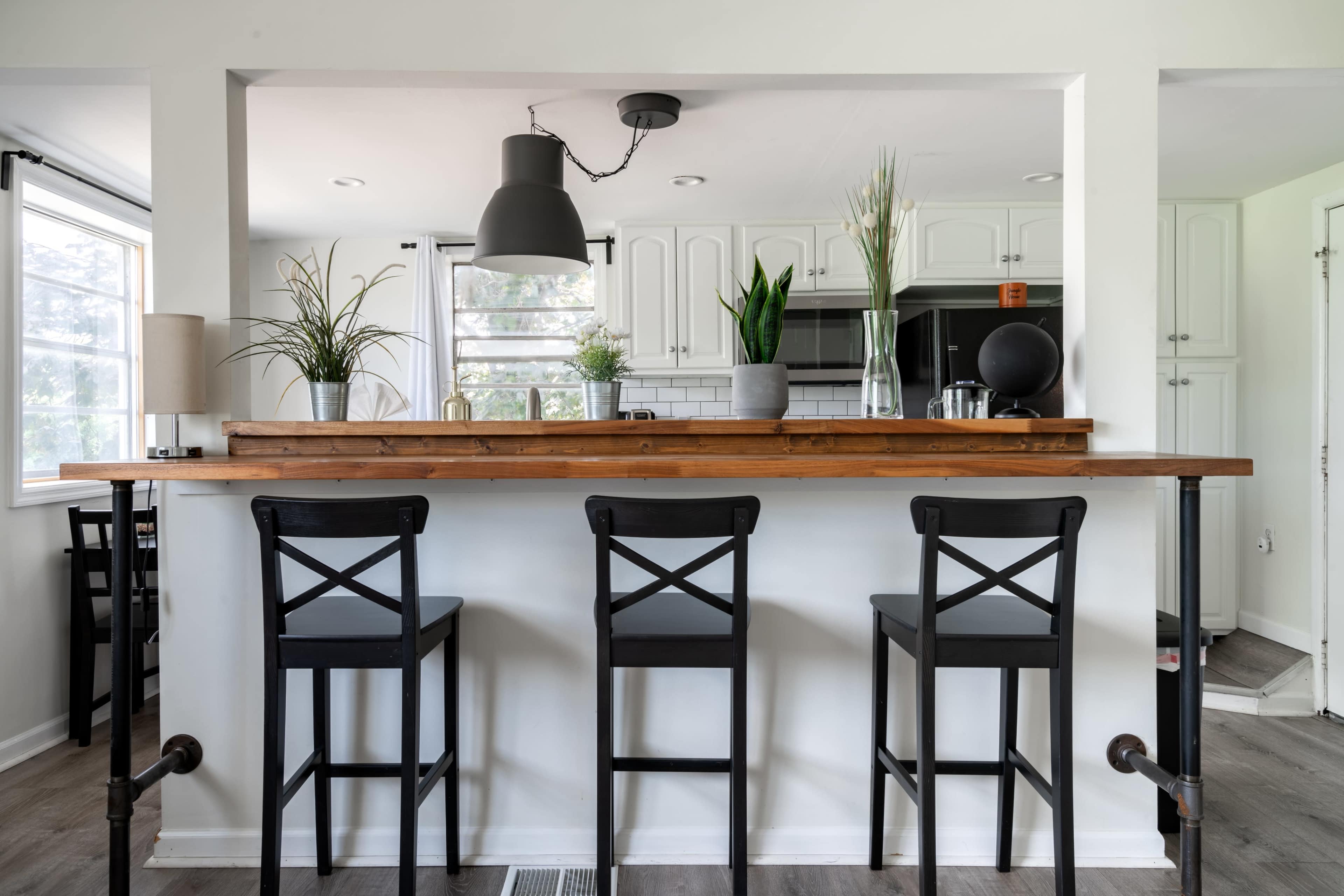 The image shows a modern kitchen with a bar area featuring three black stools and a wooden countertop.