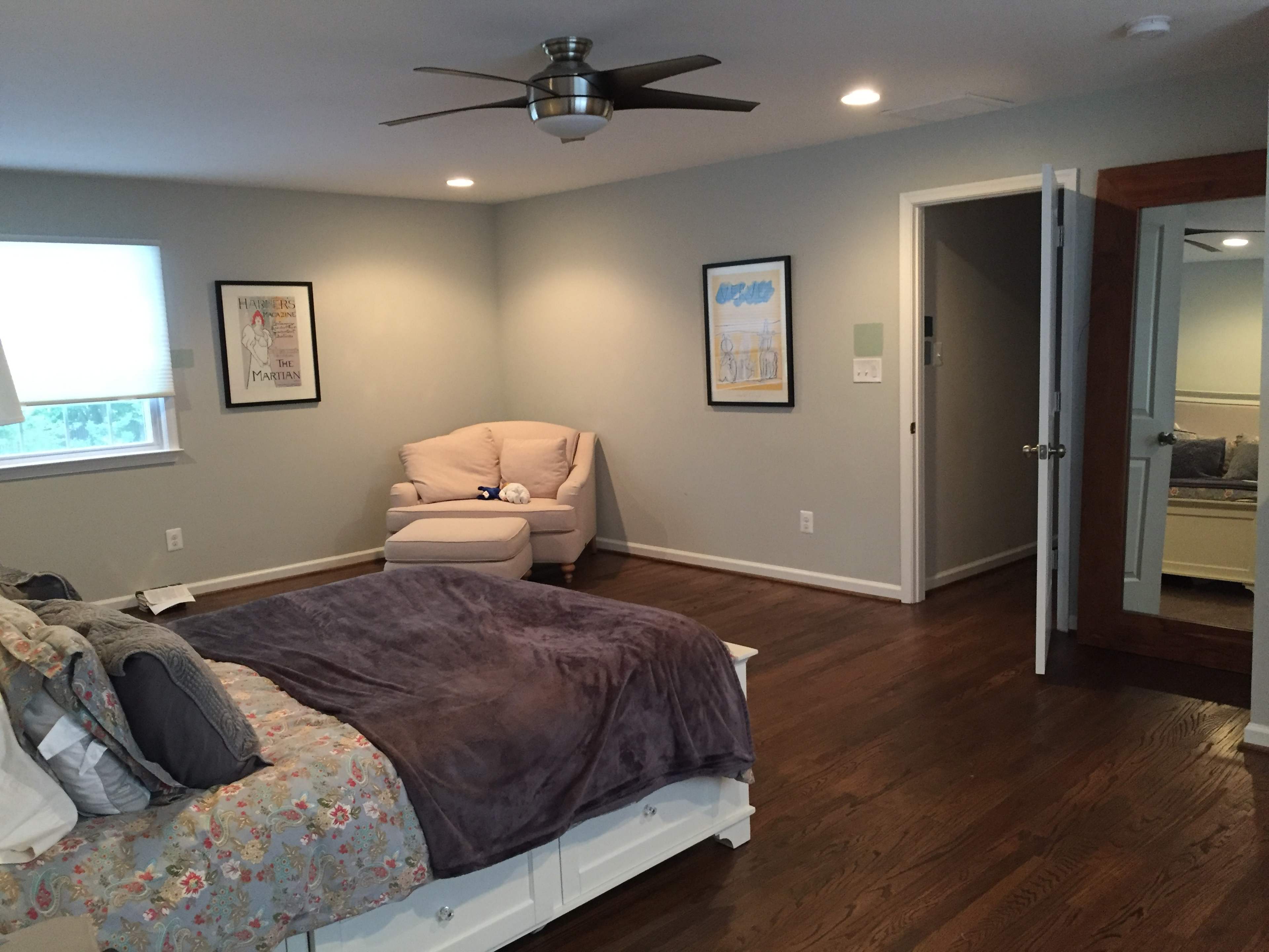 A spacious bedroom with a large bed, a beige armchair in one corner, and a mirrored closet door.