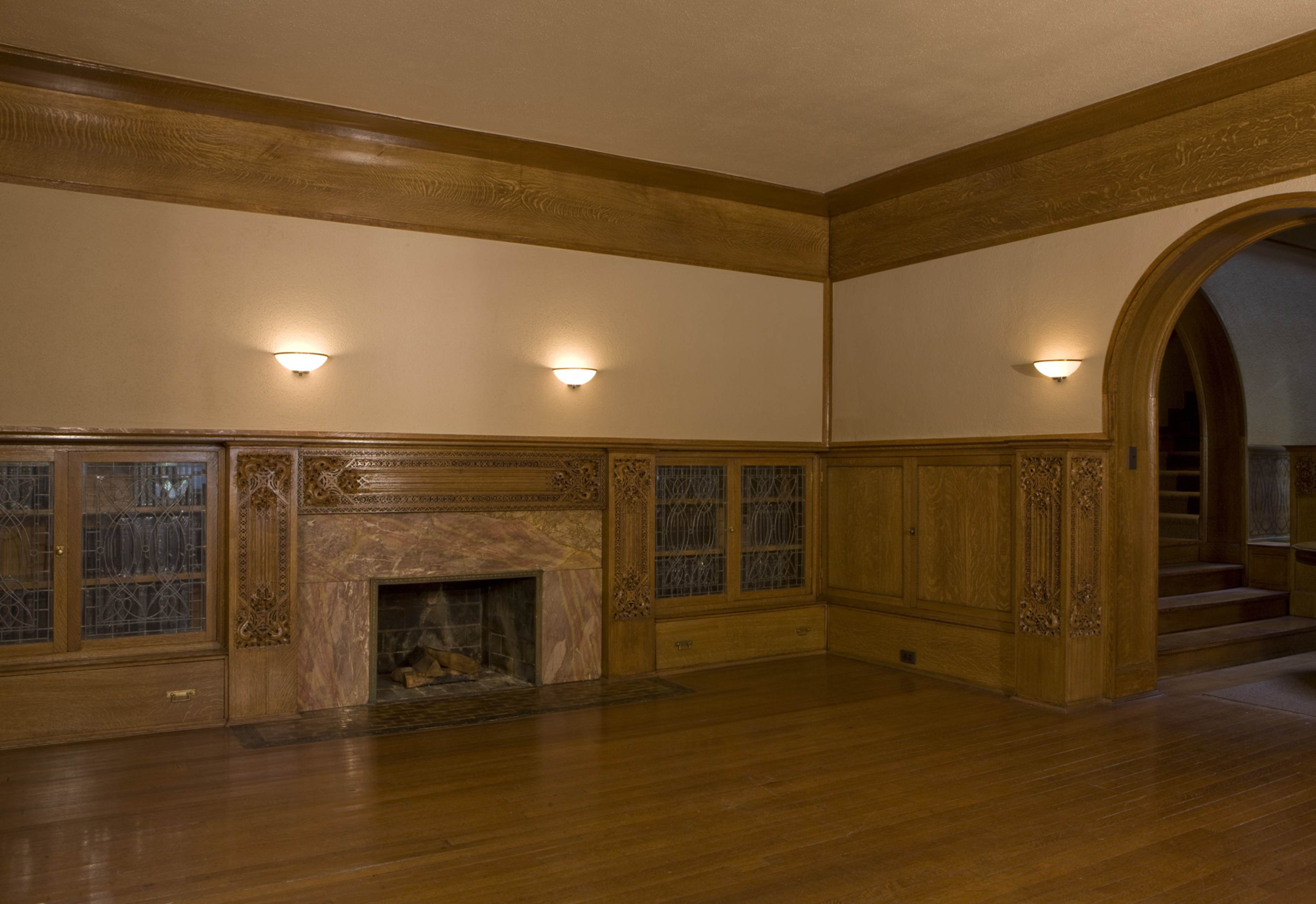 An empty room with wooden paneling, a fireplace, and archways leading to other areas.