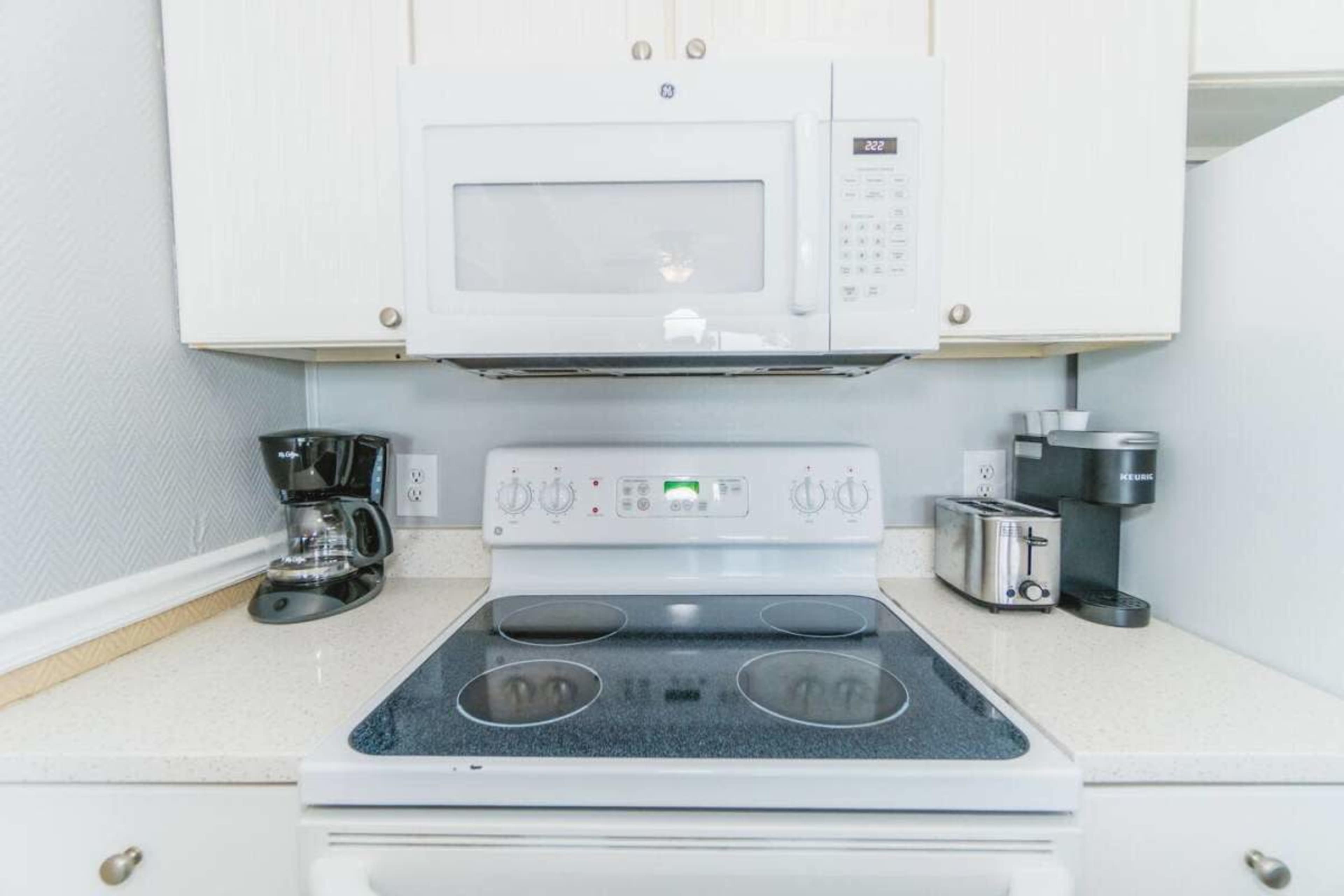 The image shows a kitchen countertop equipped with a microwave, electric stove, coffee maker, and toaster.