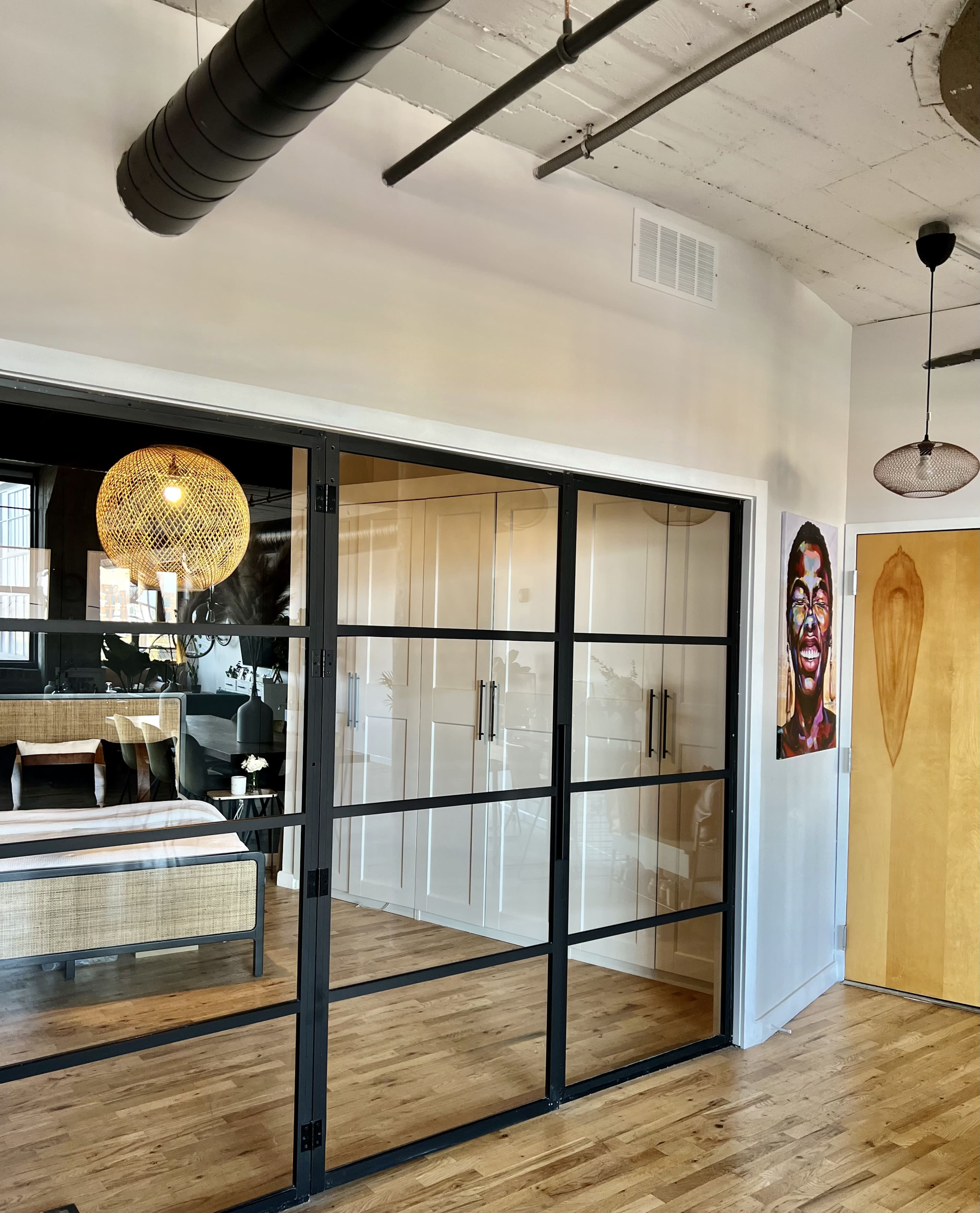 A modern interior space featuring a glass-paneled door leading to a bedroom with a stylish light fixture and a vibrant wall art piece.