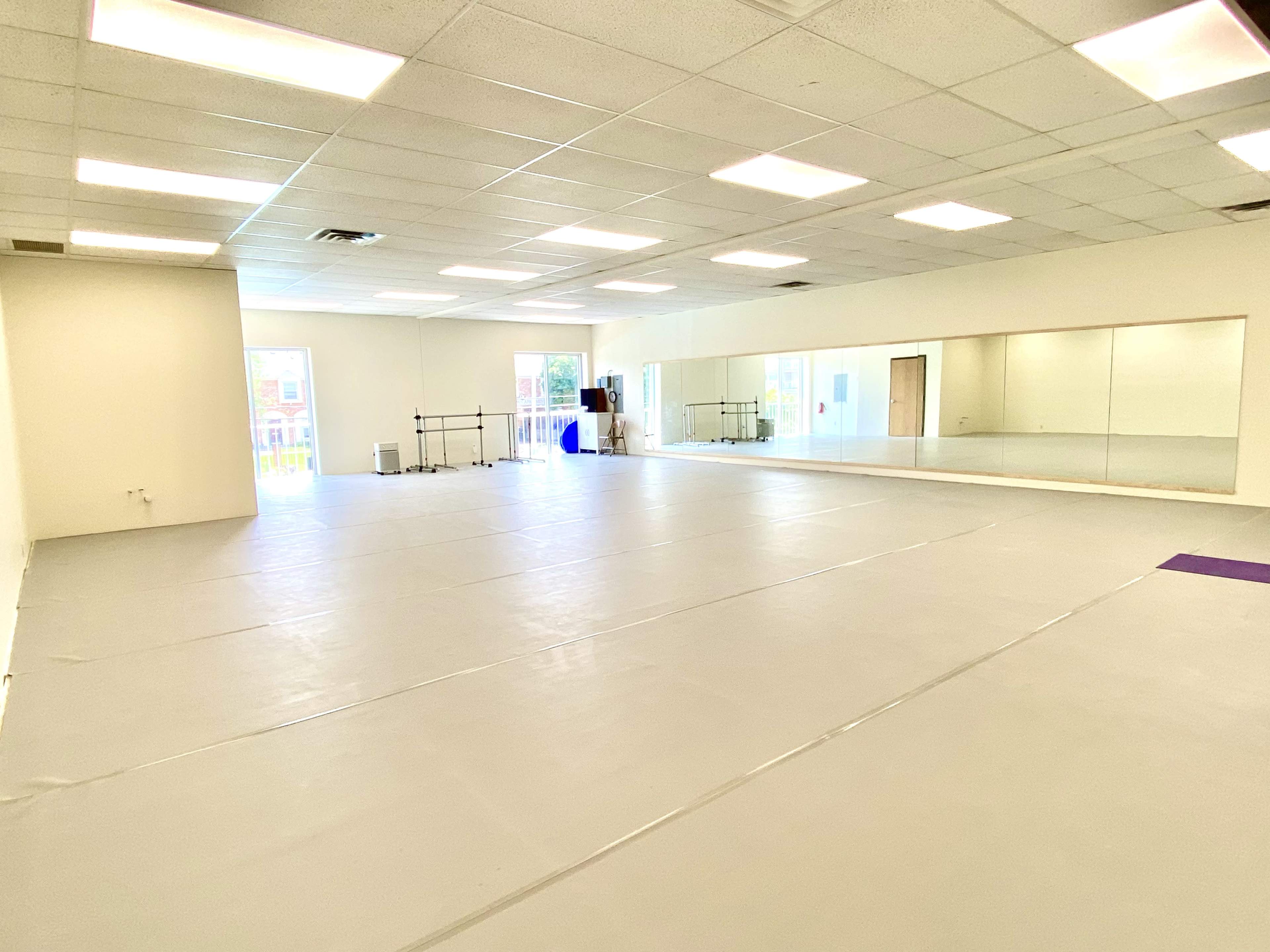 An empty studio space features a mirrored wall, open floor, and bright overhead lighting.