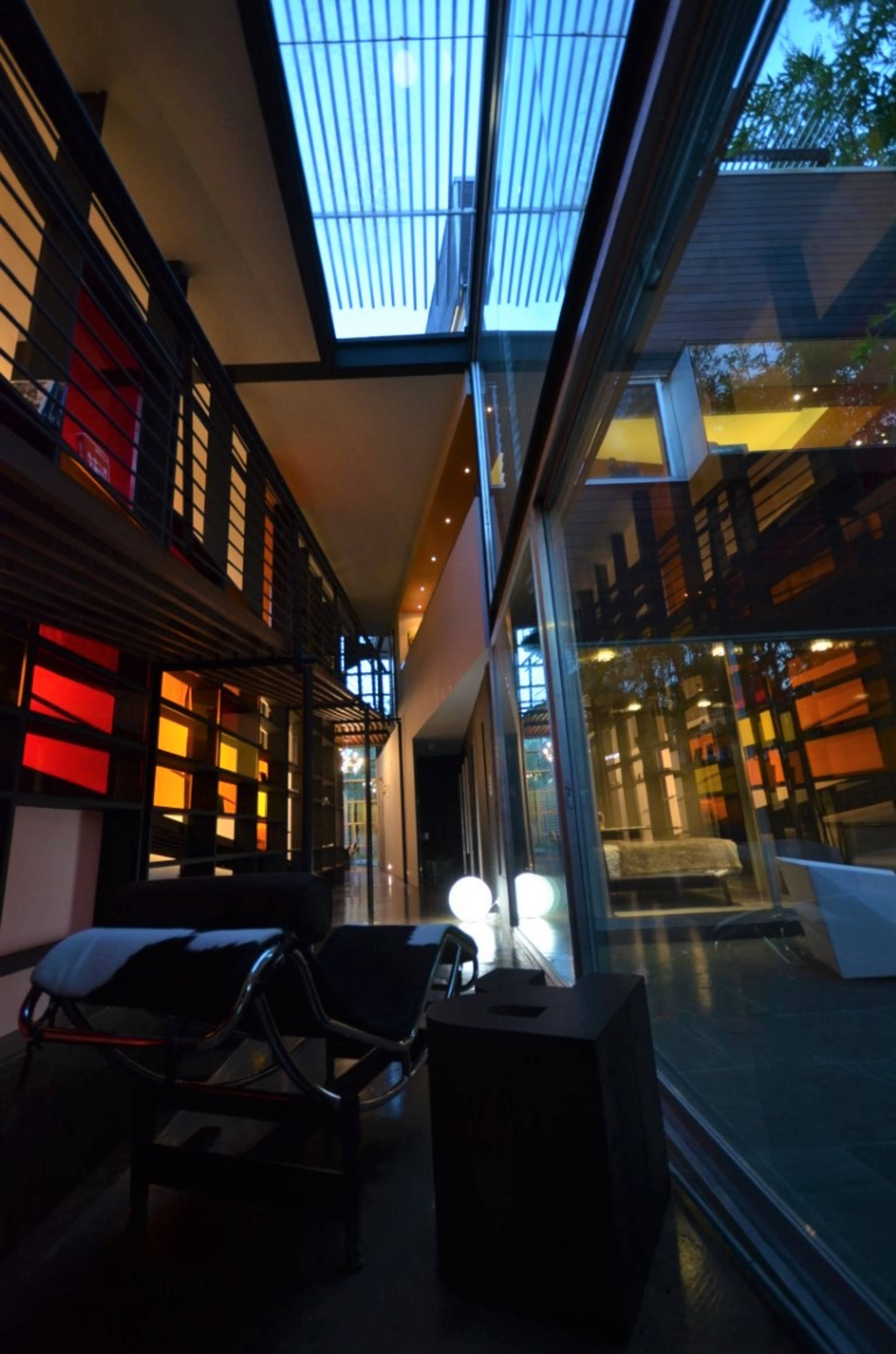 A modern interior space featuring sleek lines, large glass walls, and vibrant colored lighting, with a lounge chair positioned near a glass partition.