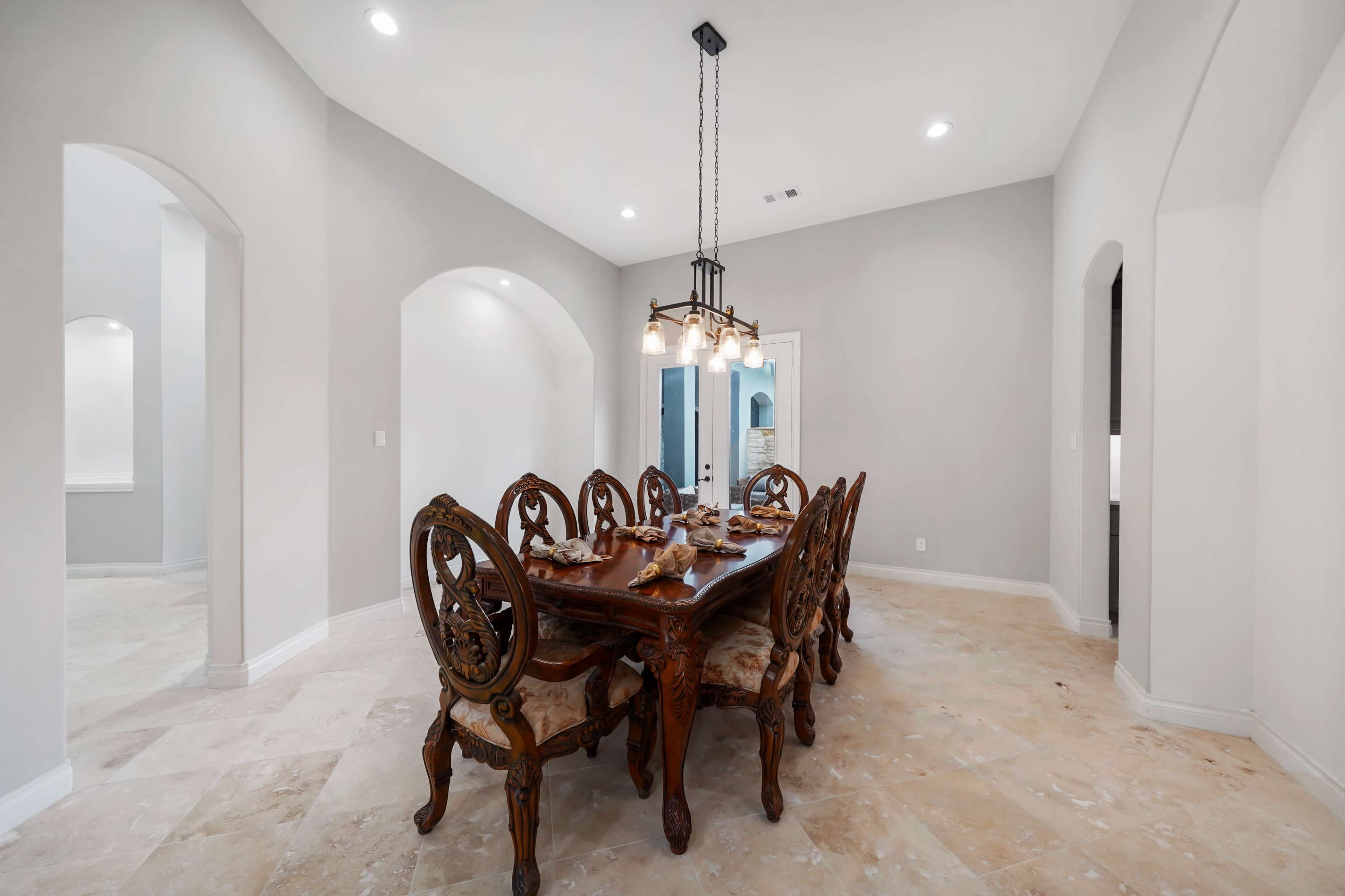 A dining room features a wooden table surrounded by six ornate chairs under a multi-light chandelier.