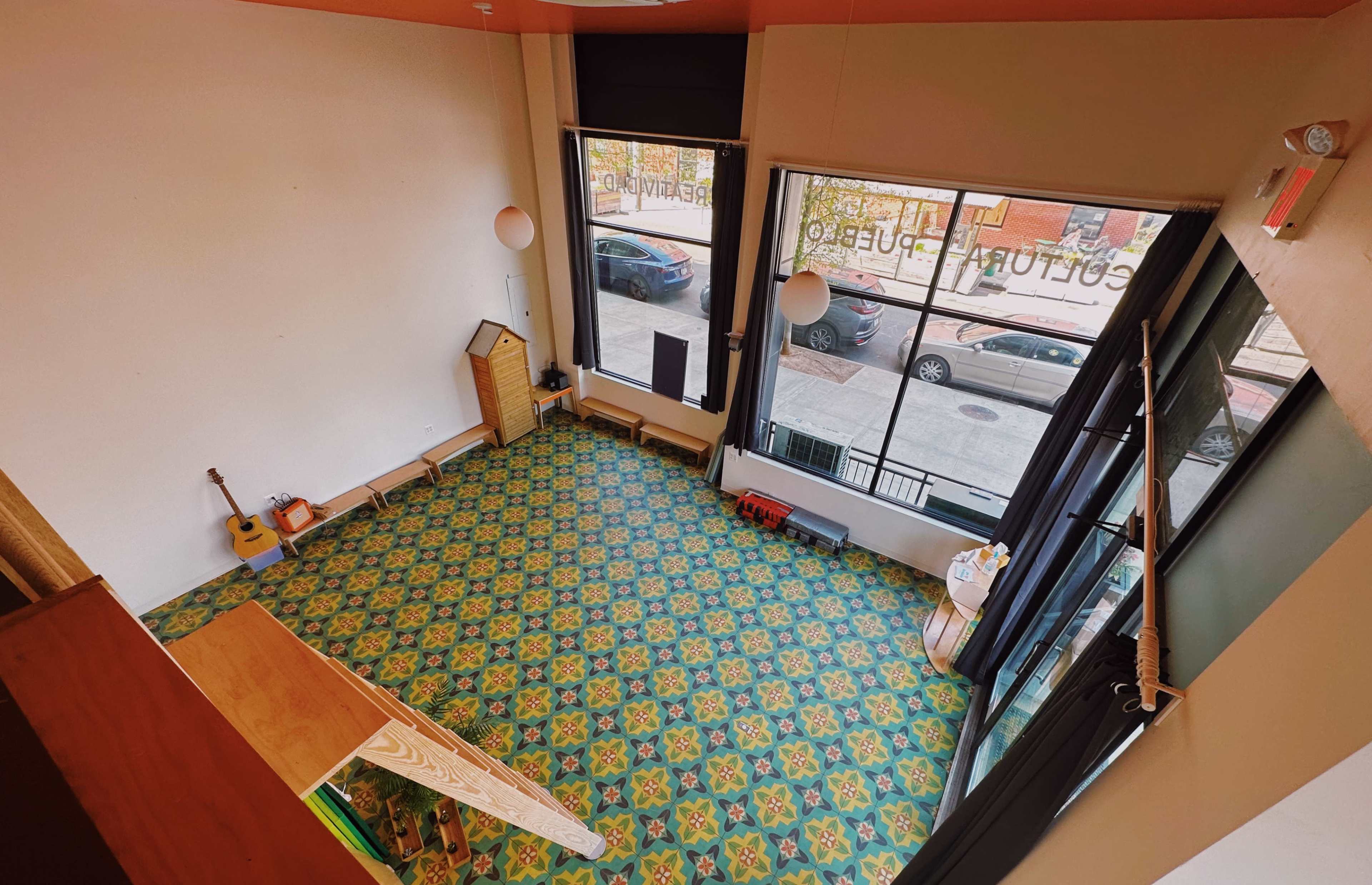 A brightly lit, empty room with a patterned floor, large windows along one wall, and some furniture arranged near the edges.