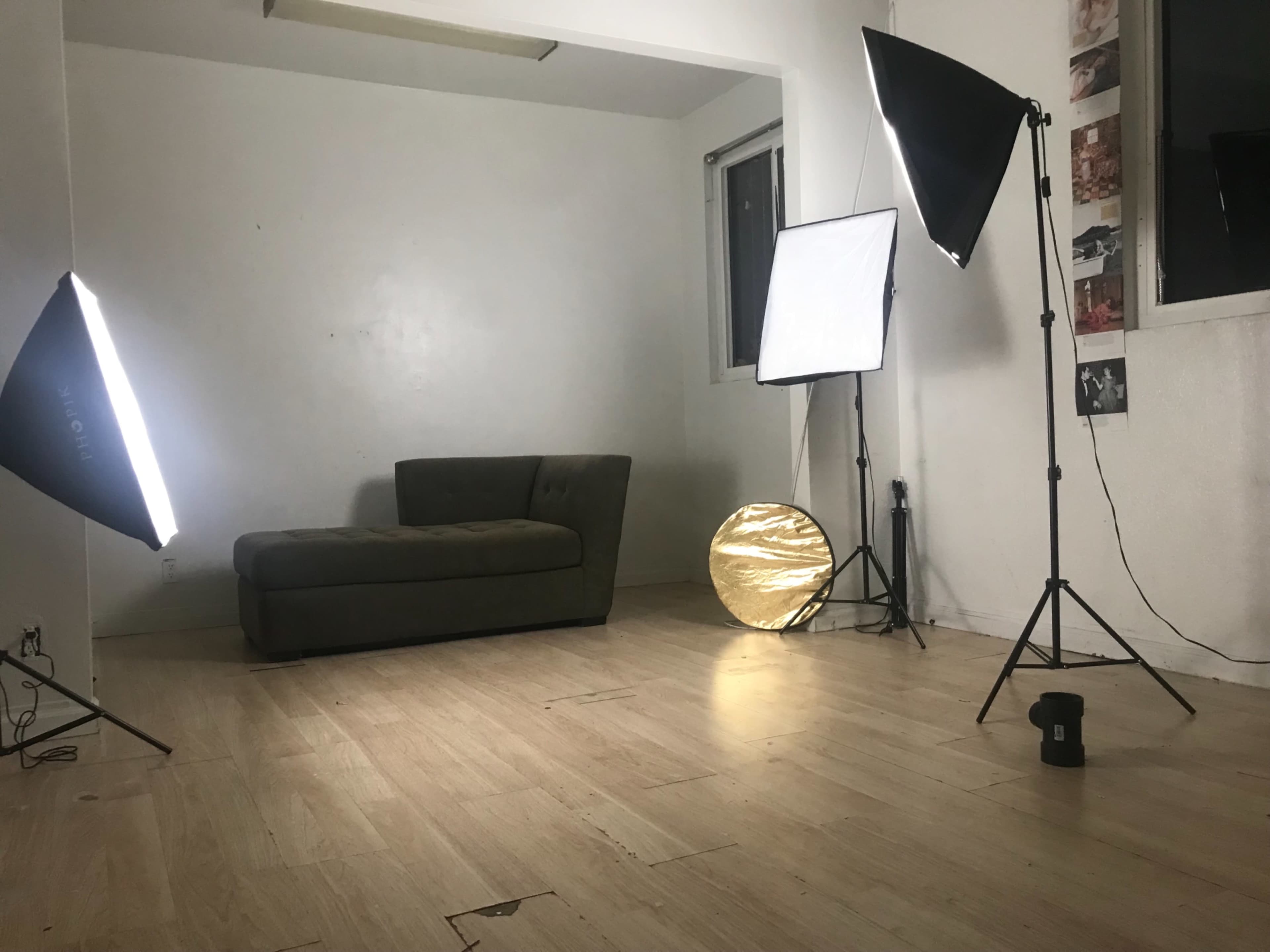 An empty room with a green couch, three lighting setups, and a gold reflector on the floor.