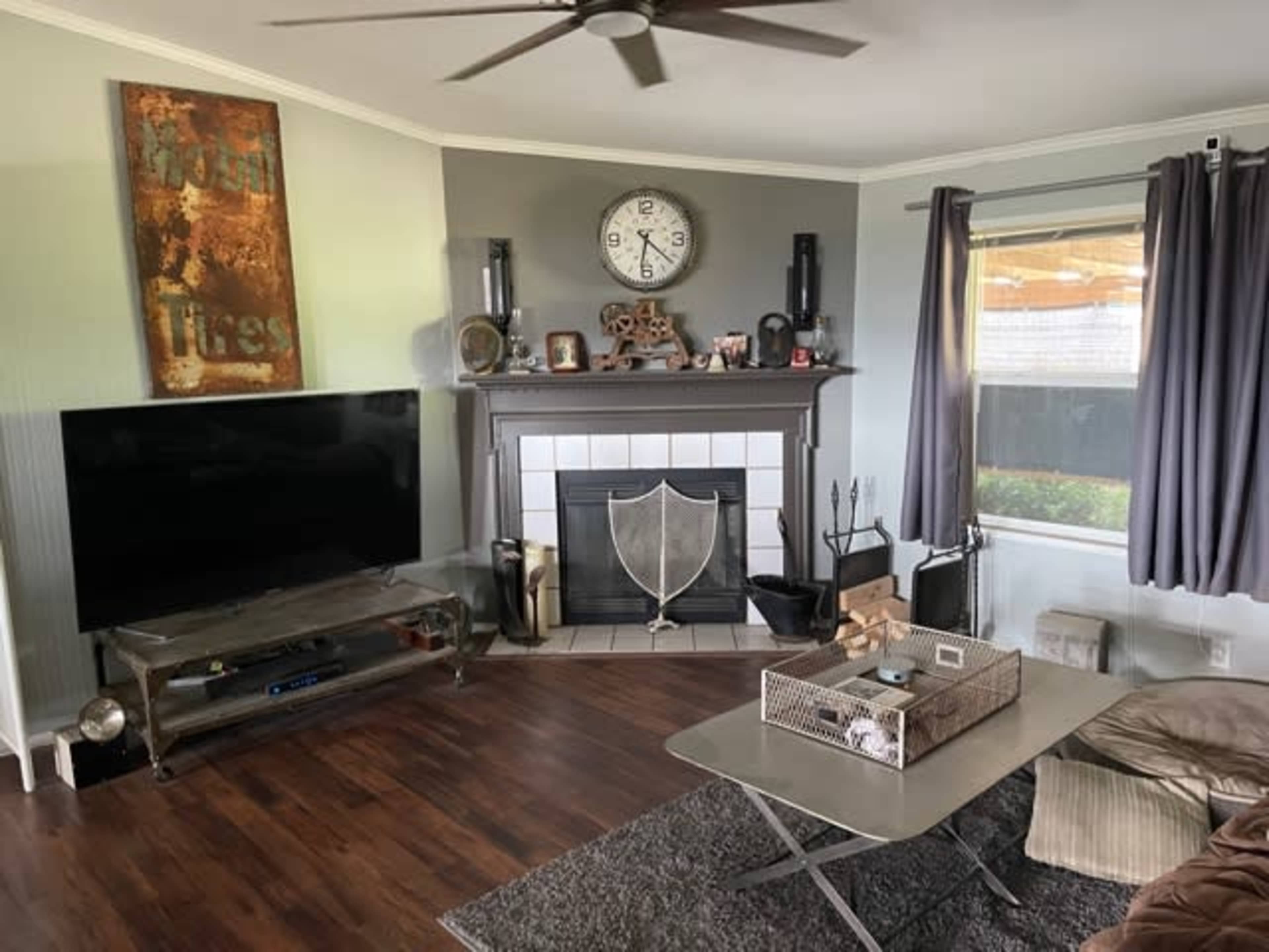 The living room features a dark wood floor, a modern TV mounted on the wall opposite a fireplace, and a coffee table with a decorative basket on it.