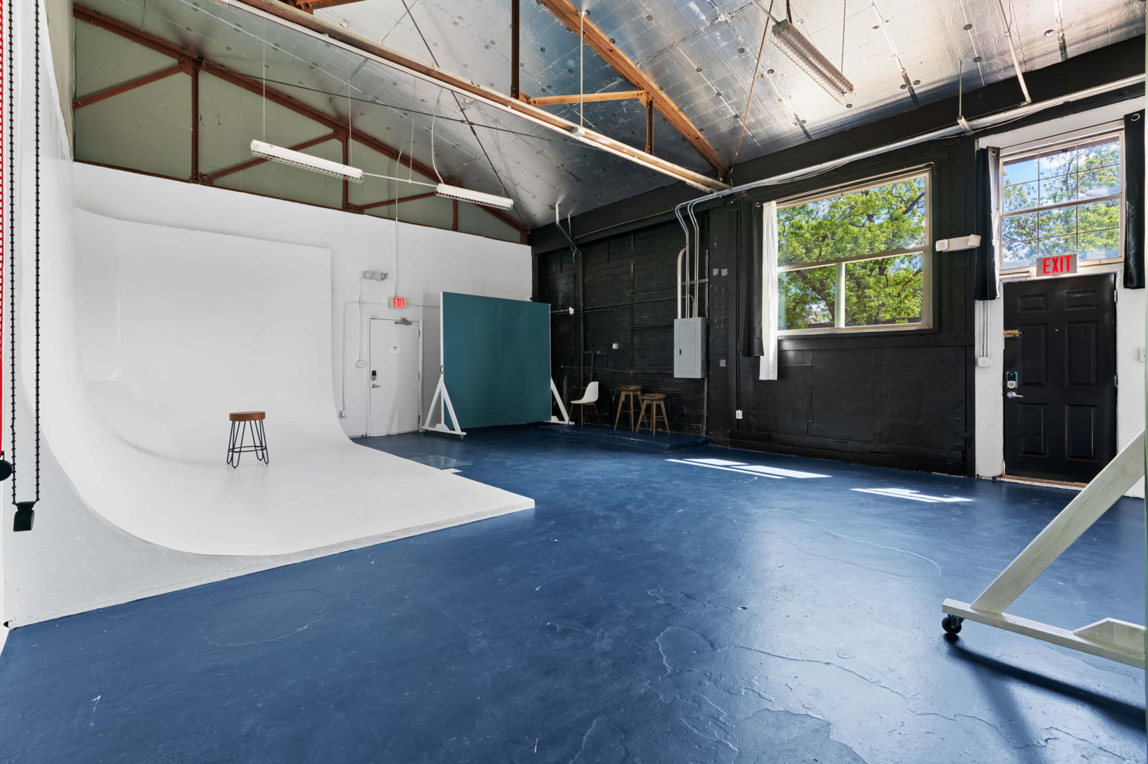A spacious photography studio with a white backdrop, a blue floor, and several pieces of studio equipment.