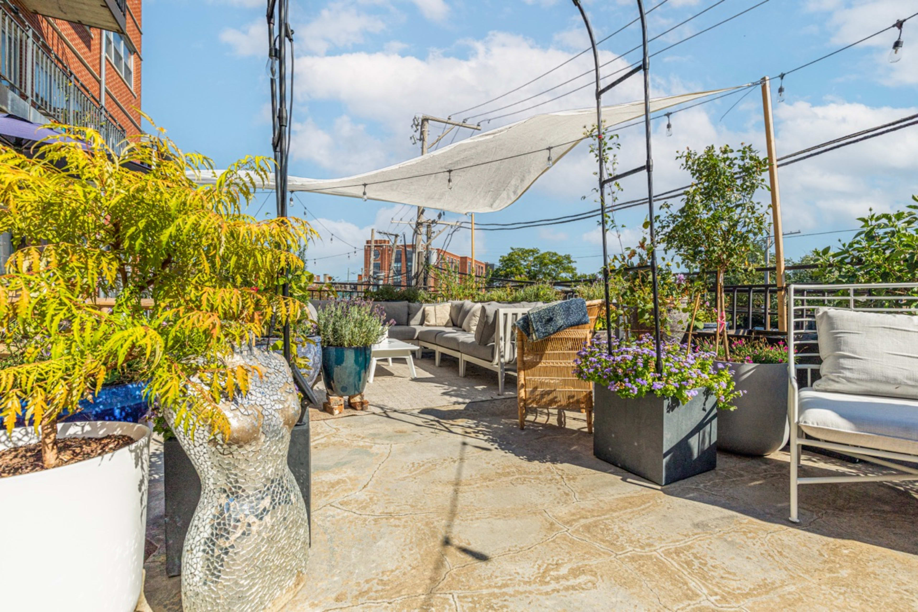 The rooftop terrace features a variety of potted plants, comfortable seating, and a shade sail providing cover from overhead.