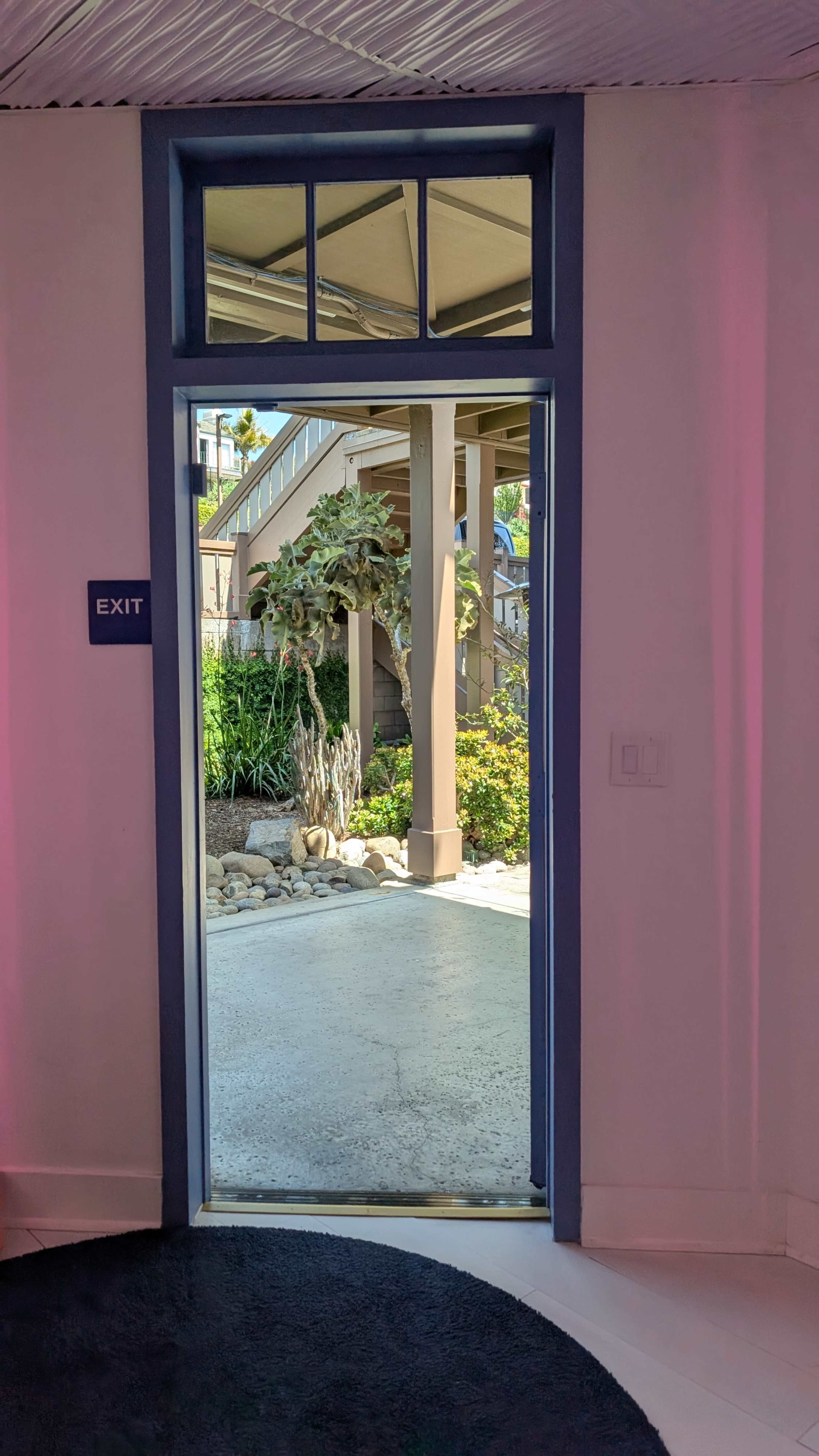 The image shows an open door labeled "EXIT" leading to a garden area with plants and a pathway.
