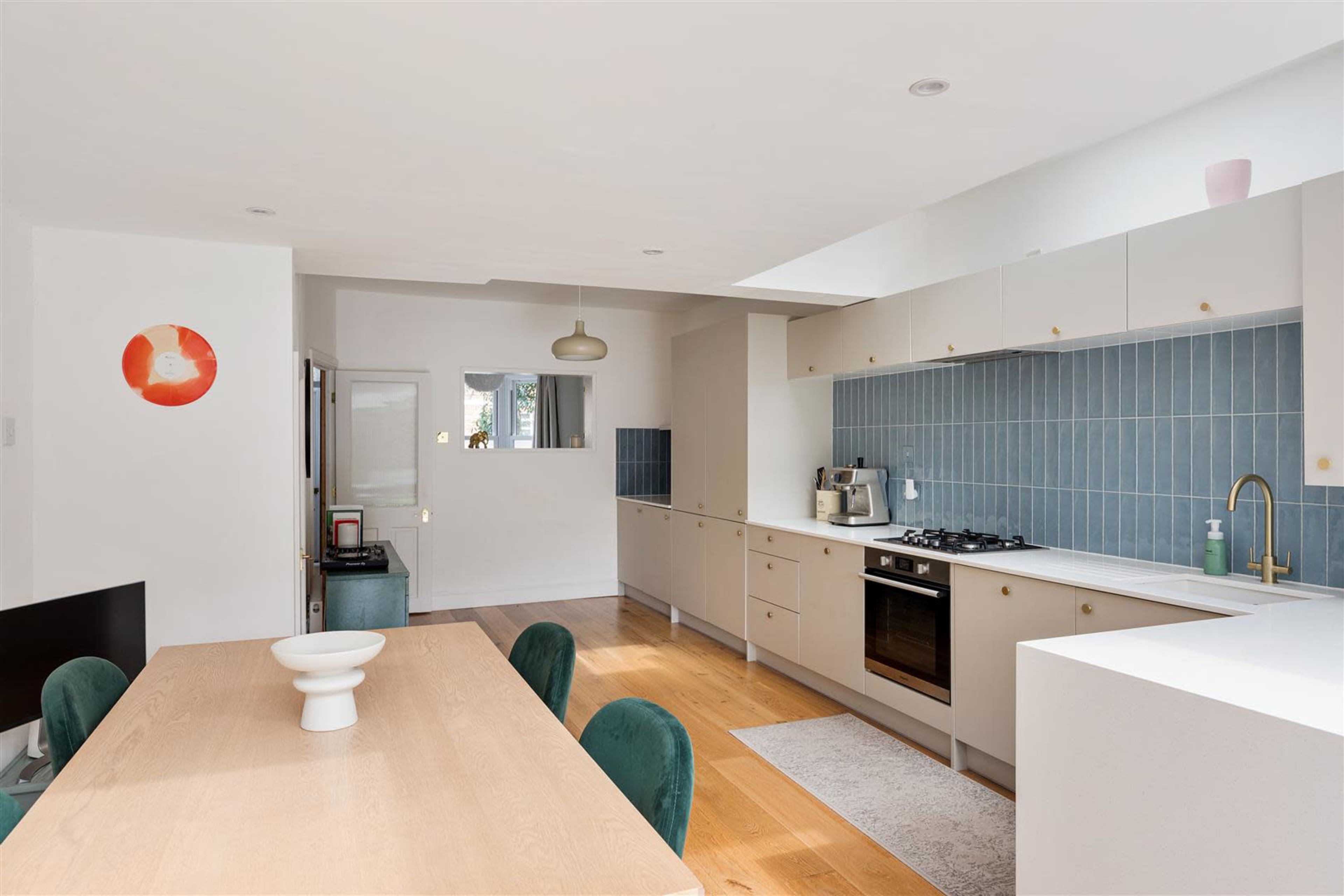 A modern kitchen features a long countertop with a gas stove, cabinetry, and a dining table with green chairs.