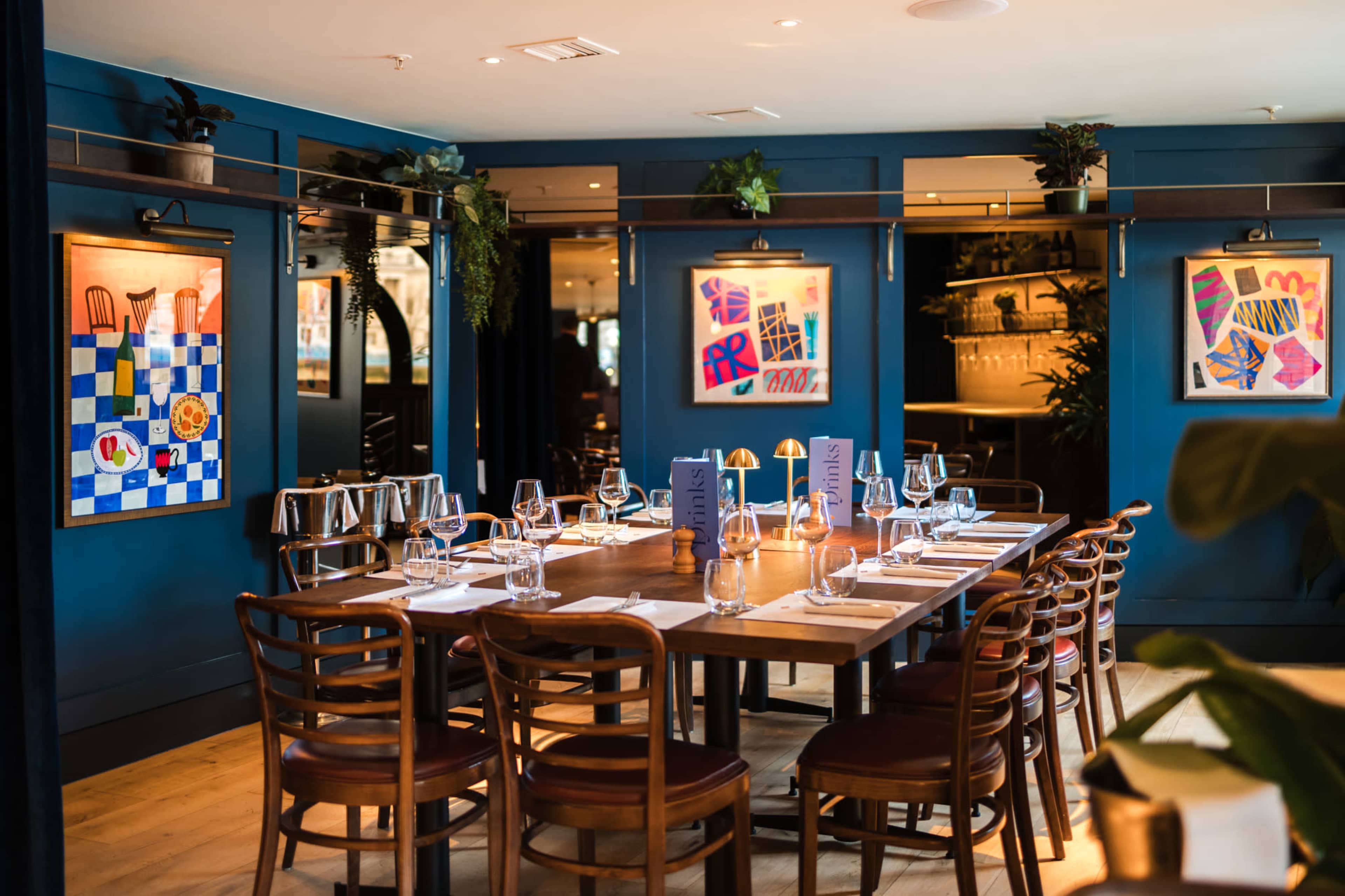 The image shows a neatly arranged dining table in a restaurant with blue walls adorned with framed artwork.