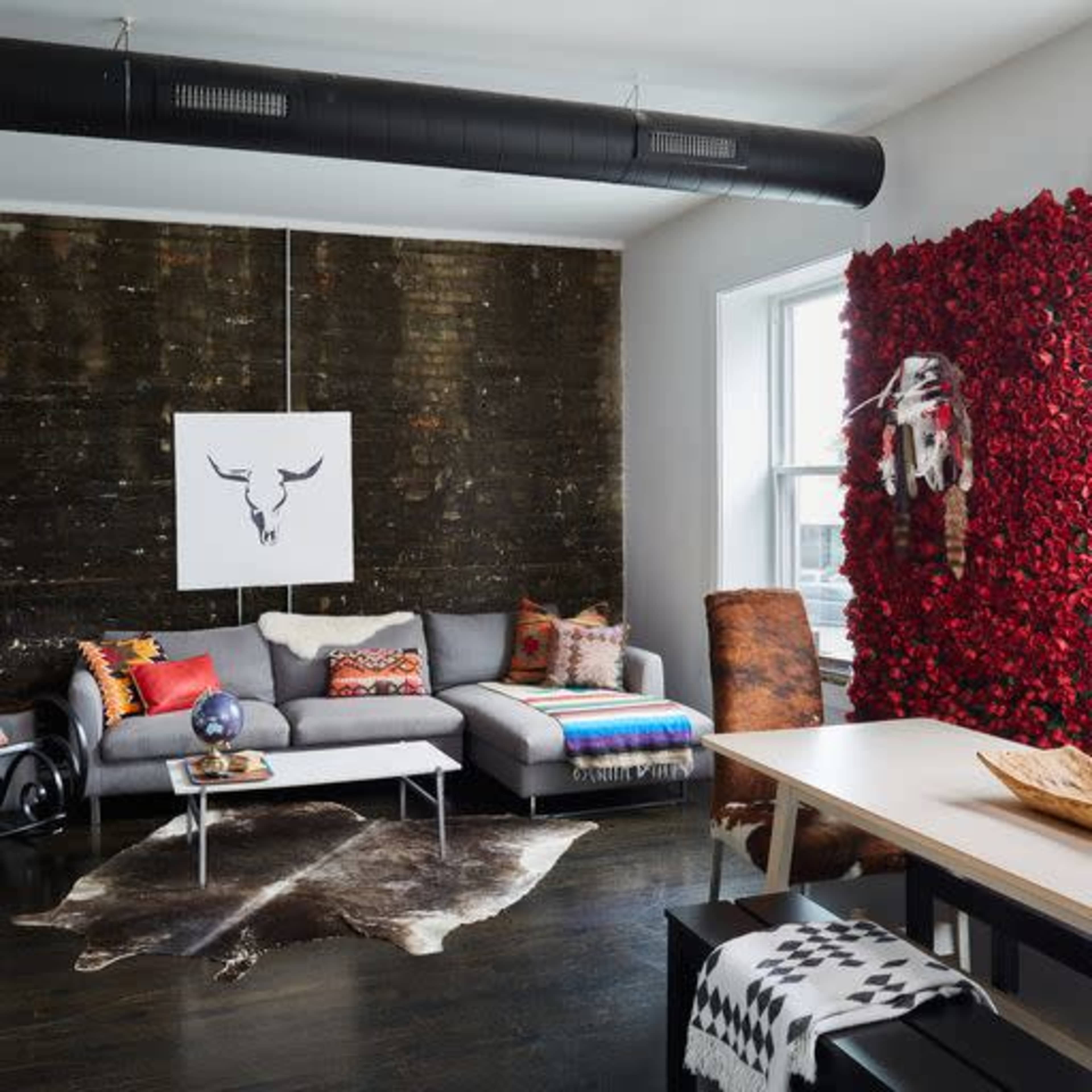 A modern living area features a sectional couch, a round coffee table, and a dining table against a backdrop of a textured wall and a decorative floral accent wall.
