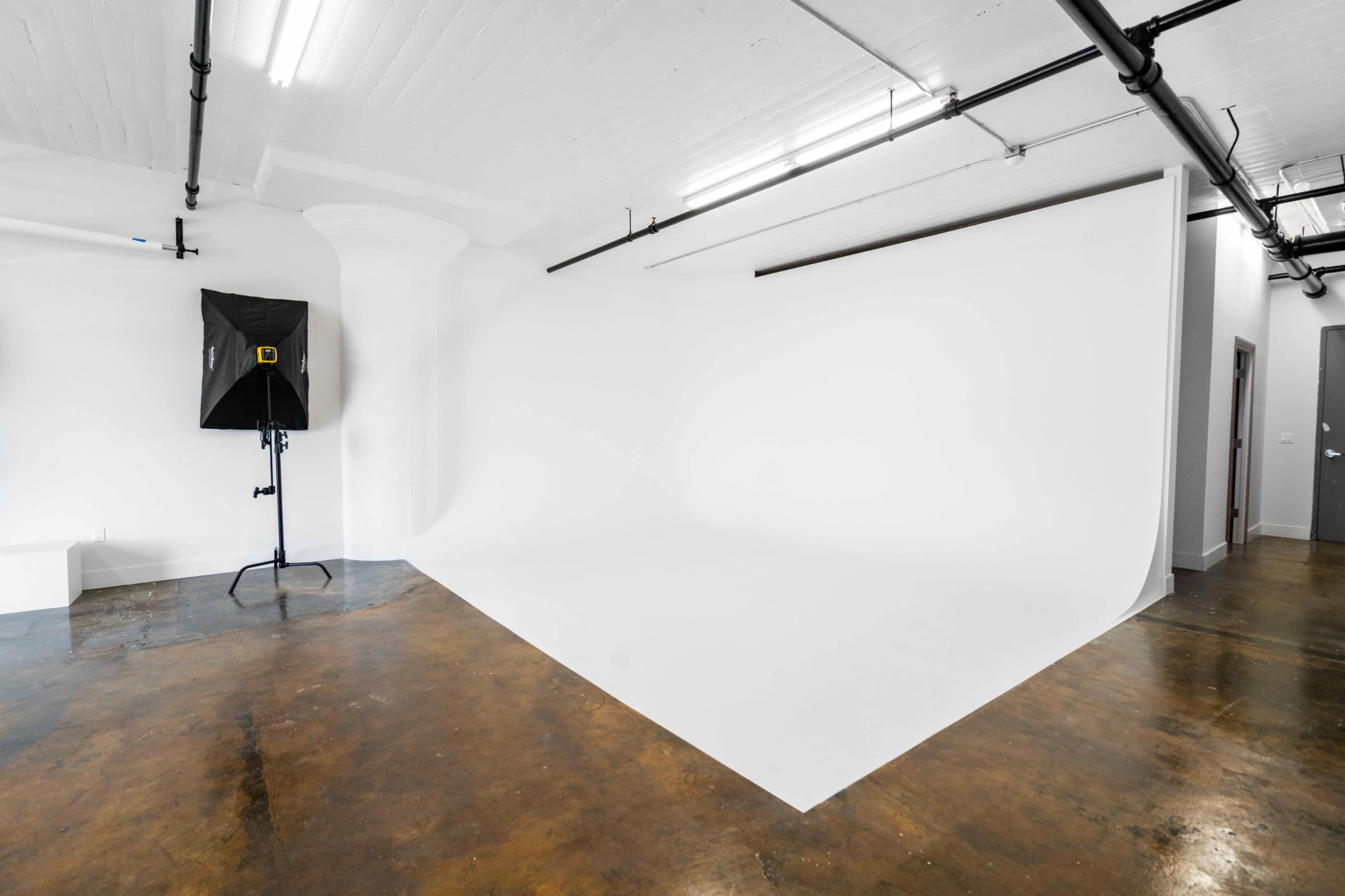 A photography studio features a seamless white backdrop and studio lighting equipment in a spacious, brightly lit room.