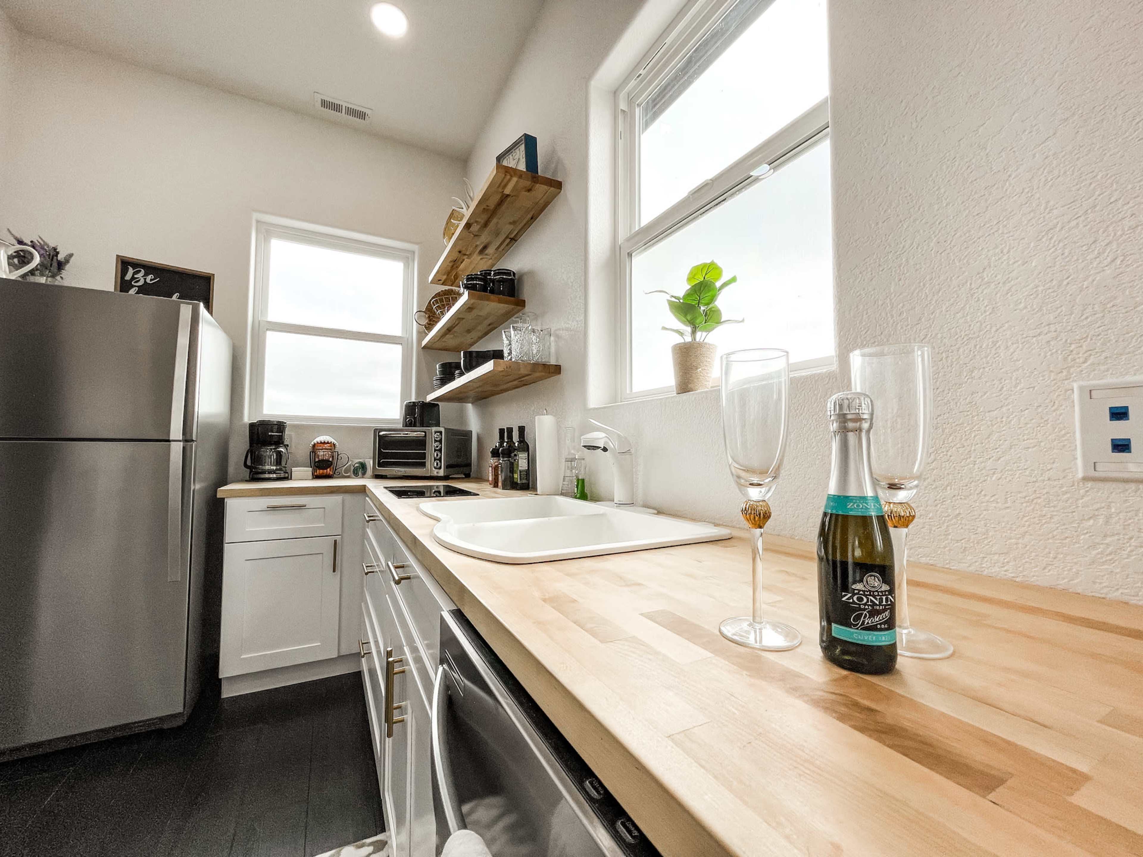 A well-organized kitchen featuring a stainless steel refrigerator, wooden countertop, and a bottle of sparkling wine with two glasses set nearby.