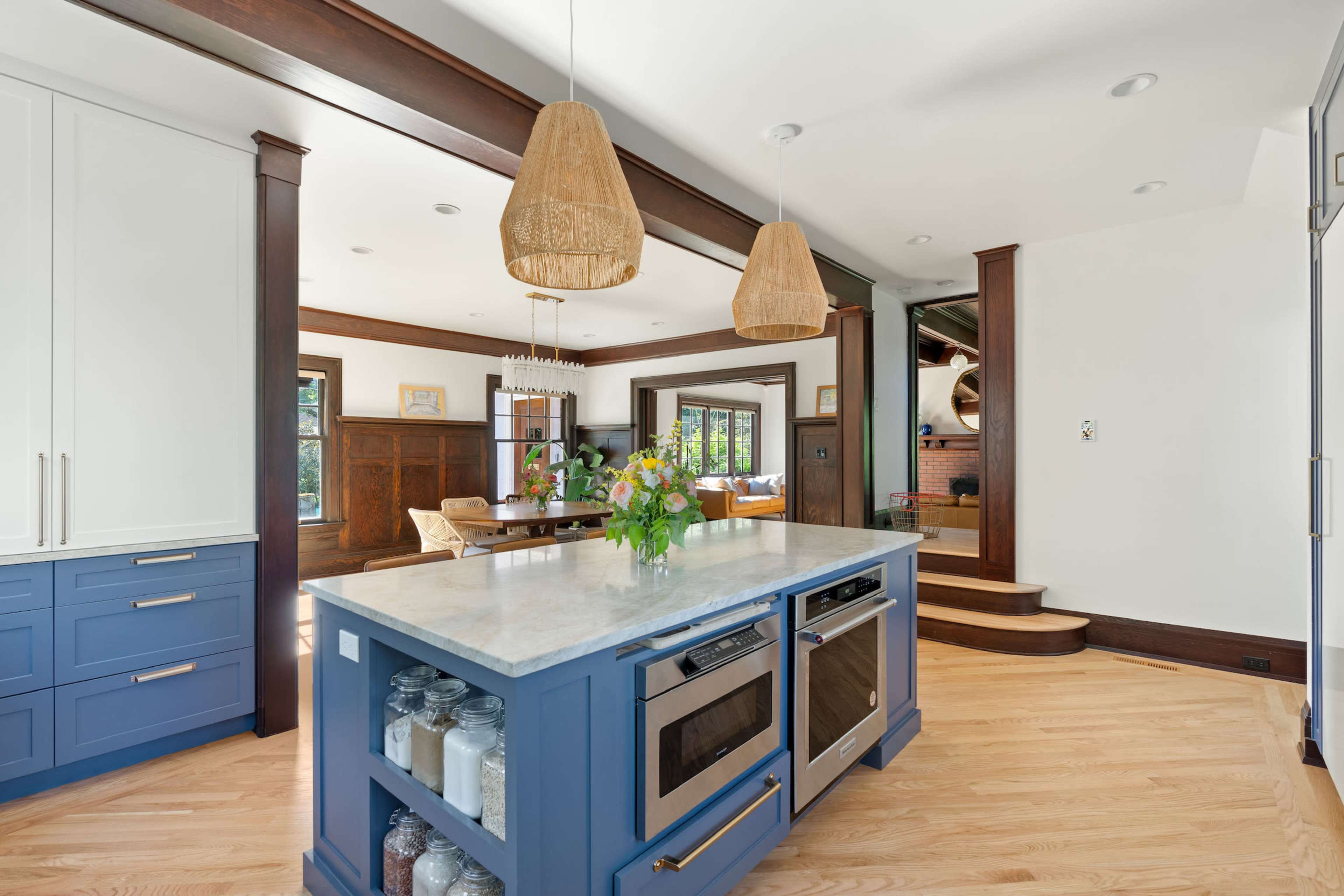 A modern kitchen features a blue island with a marble countertop, open shelves displaying jars, and pendant lights hanging above.