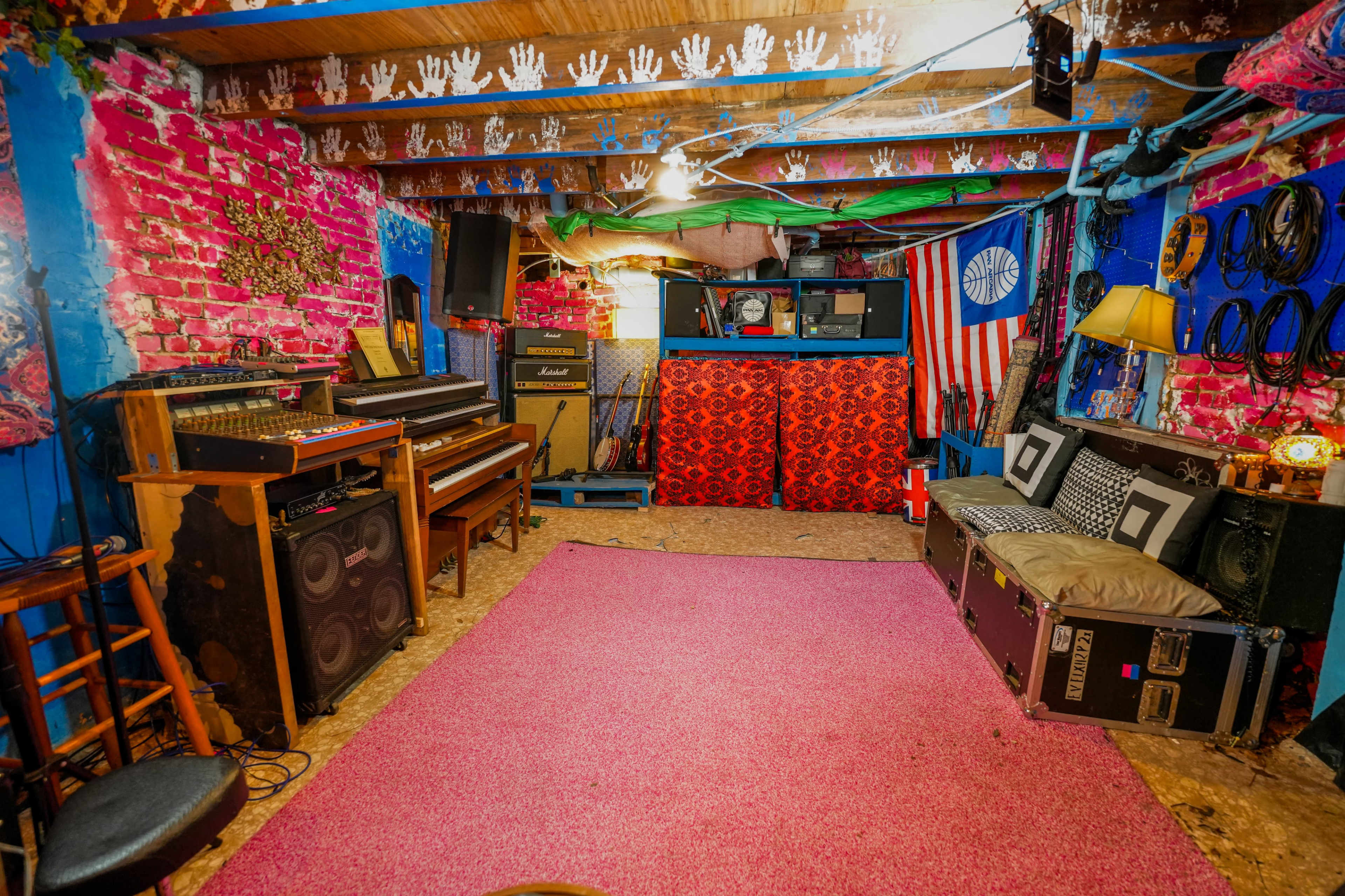 The room features colorful walls adorned with handprints, a pink carpet, musical instruments, and a small seating area with a lamp.