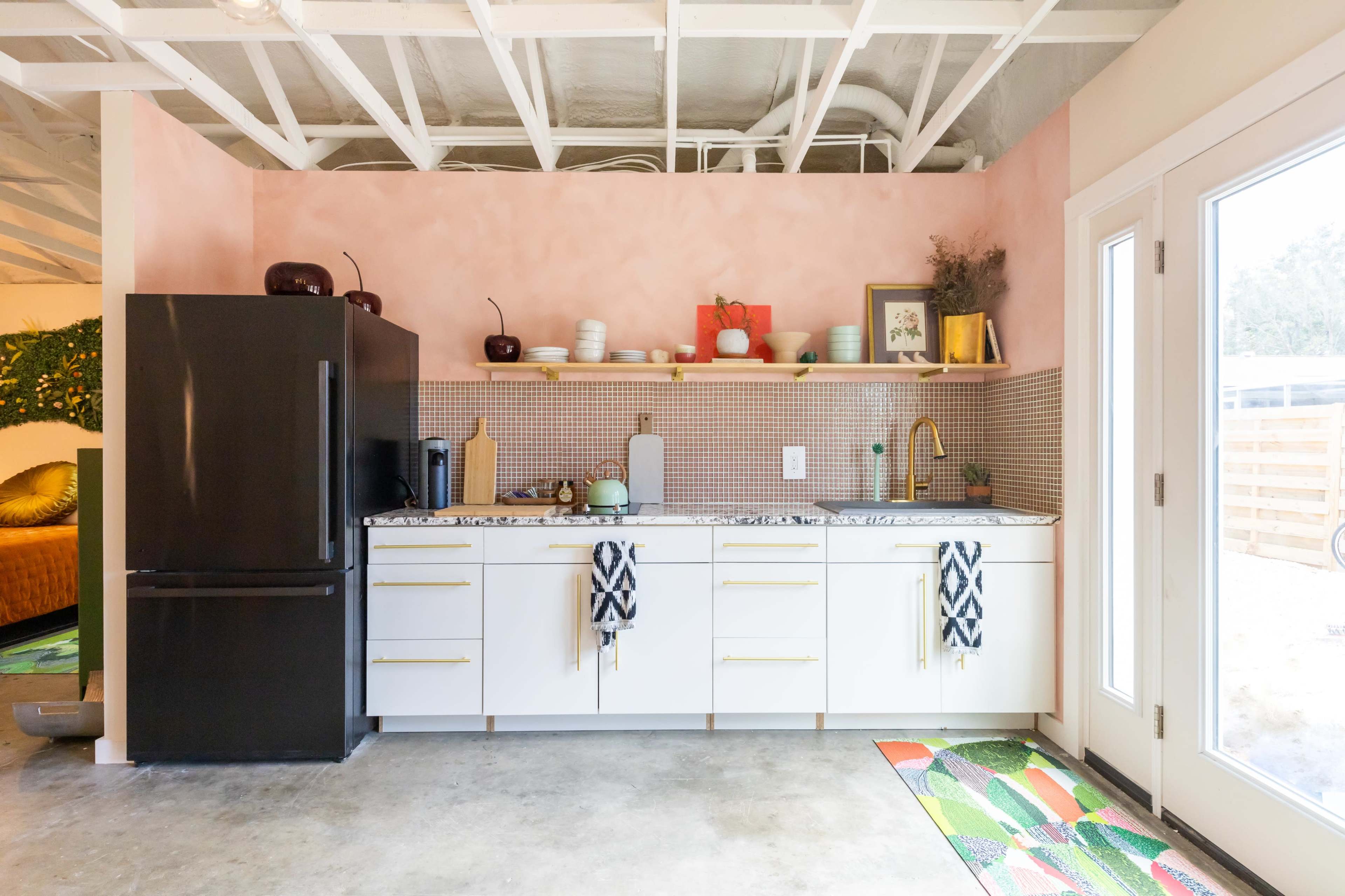 A modern kitchen with a pink wall, white cabinetry, a patterned backsplash, and a large black refrigerator.