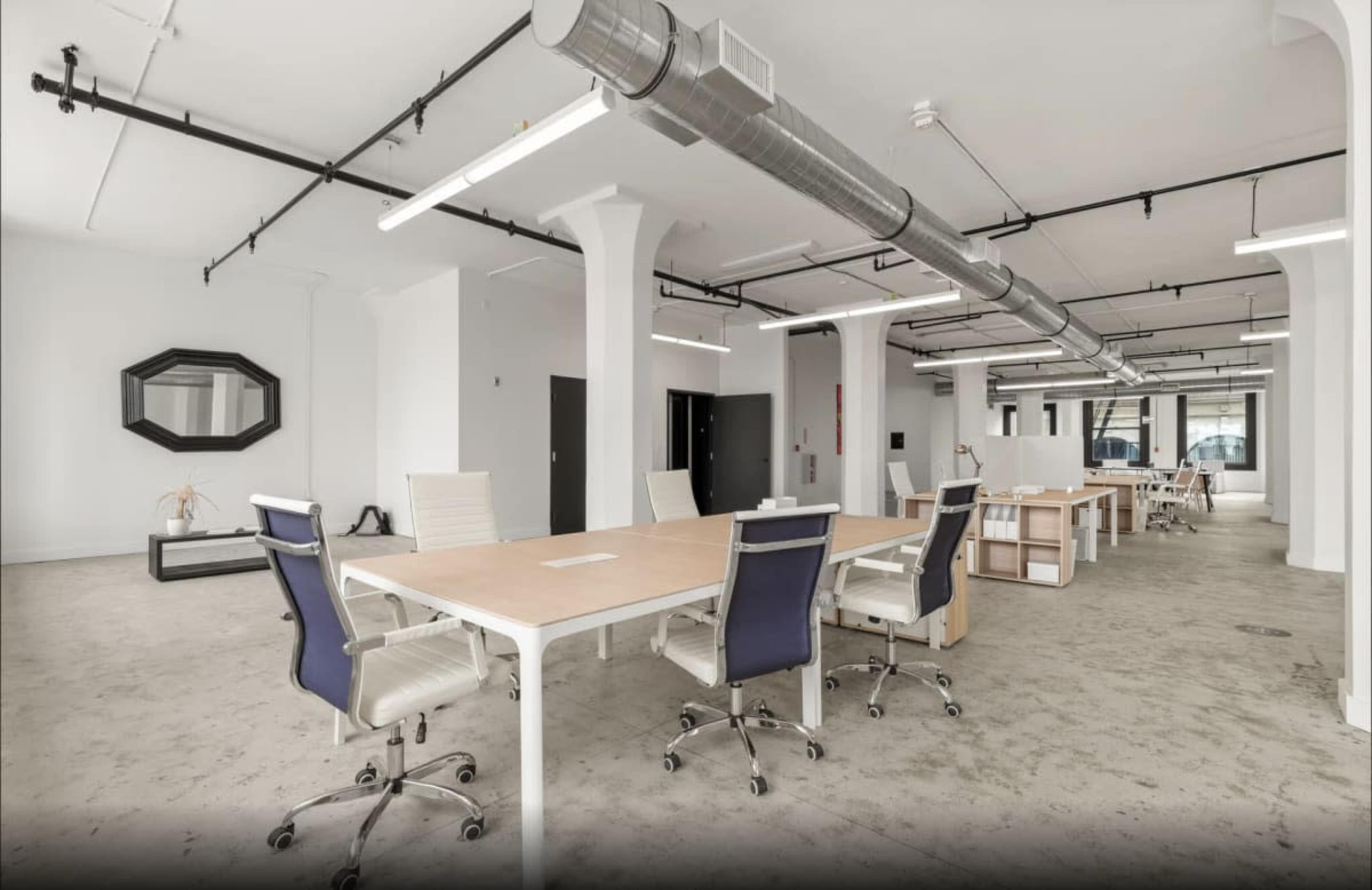 The image shows a spacious, modern office interior with large desks, ergonomic chairs, and minimalistic decor.