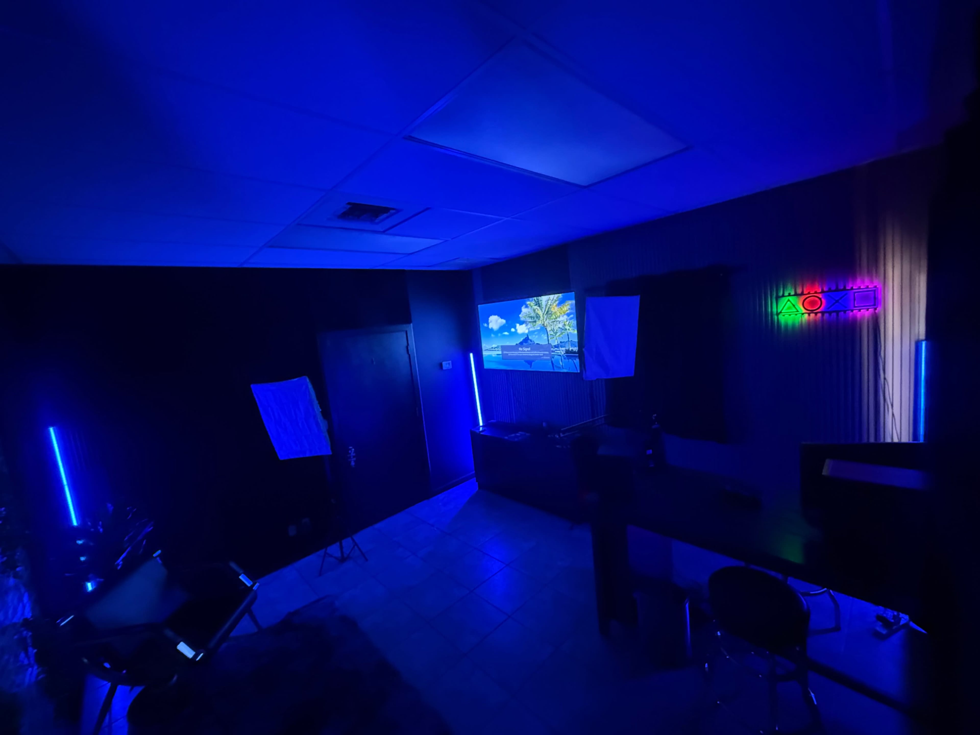 The room is illuminated in blue light, featuring a projector displaying an image on the wall, and a sleek desk with modern lighting equipment.