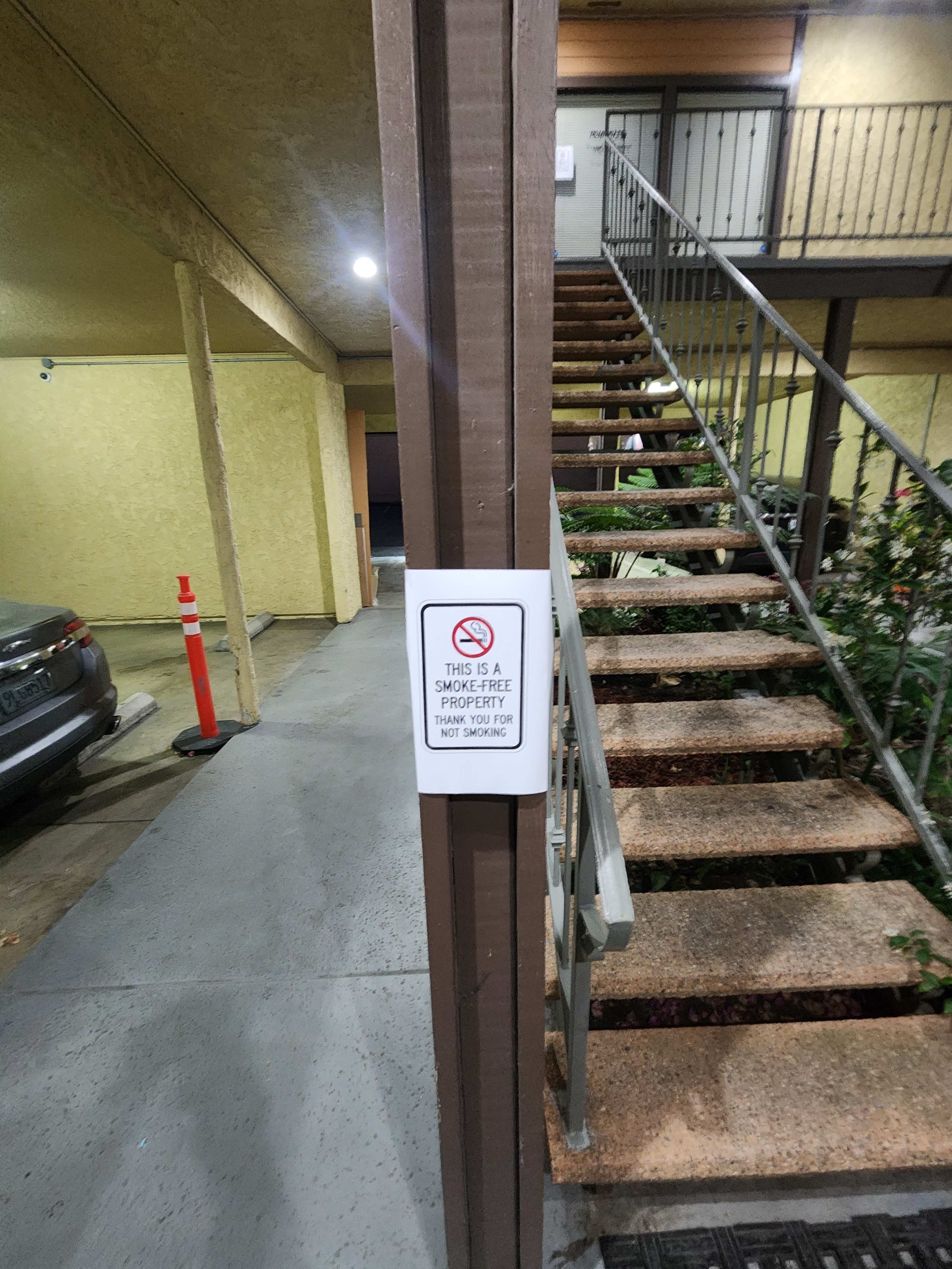A no smoking sign is posted on a wooden post beside a staircase leading to an upper level in an apartment complex.