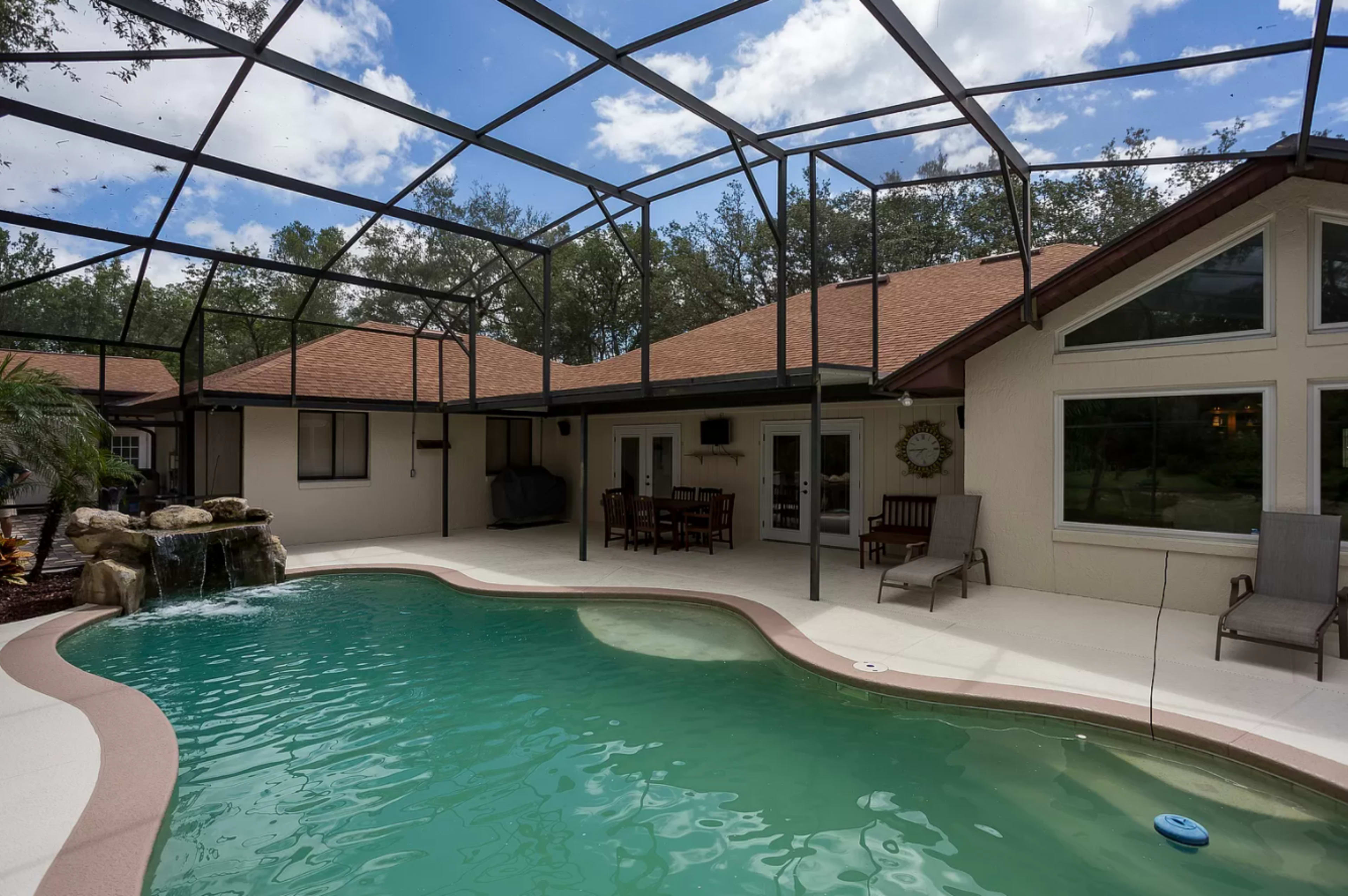 A backyard pool area enclosed by a screen, featuring a kidney-shaped pool, a rock waterfall, and a seating area with patio furniture.