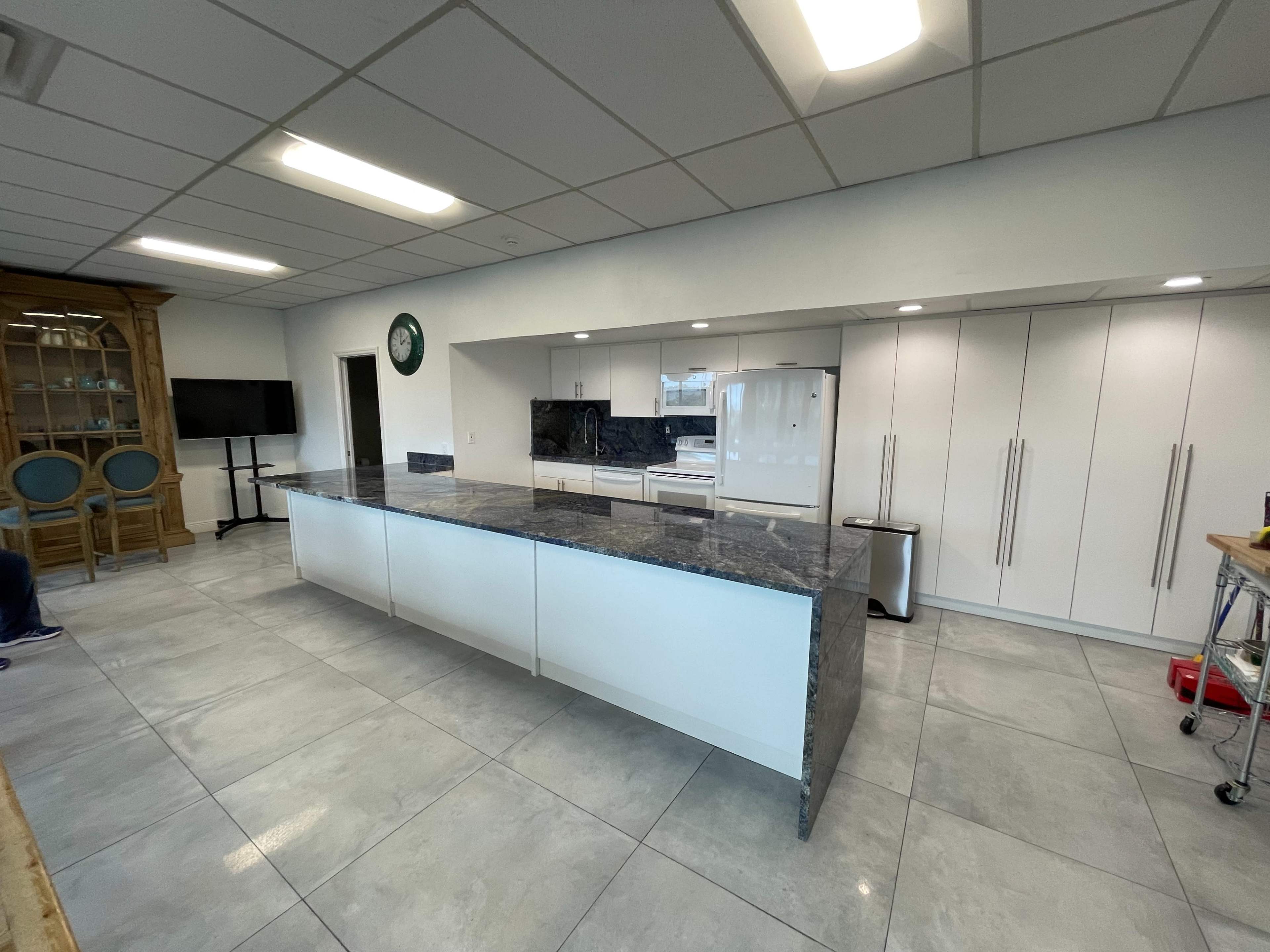 A modern kitchen with a large island, white cabinetry, and stainless steel appliances on a tiled floor.