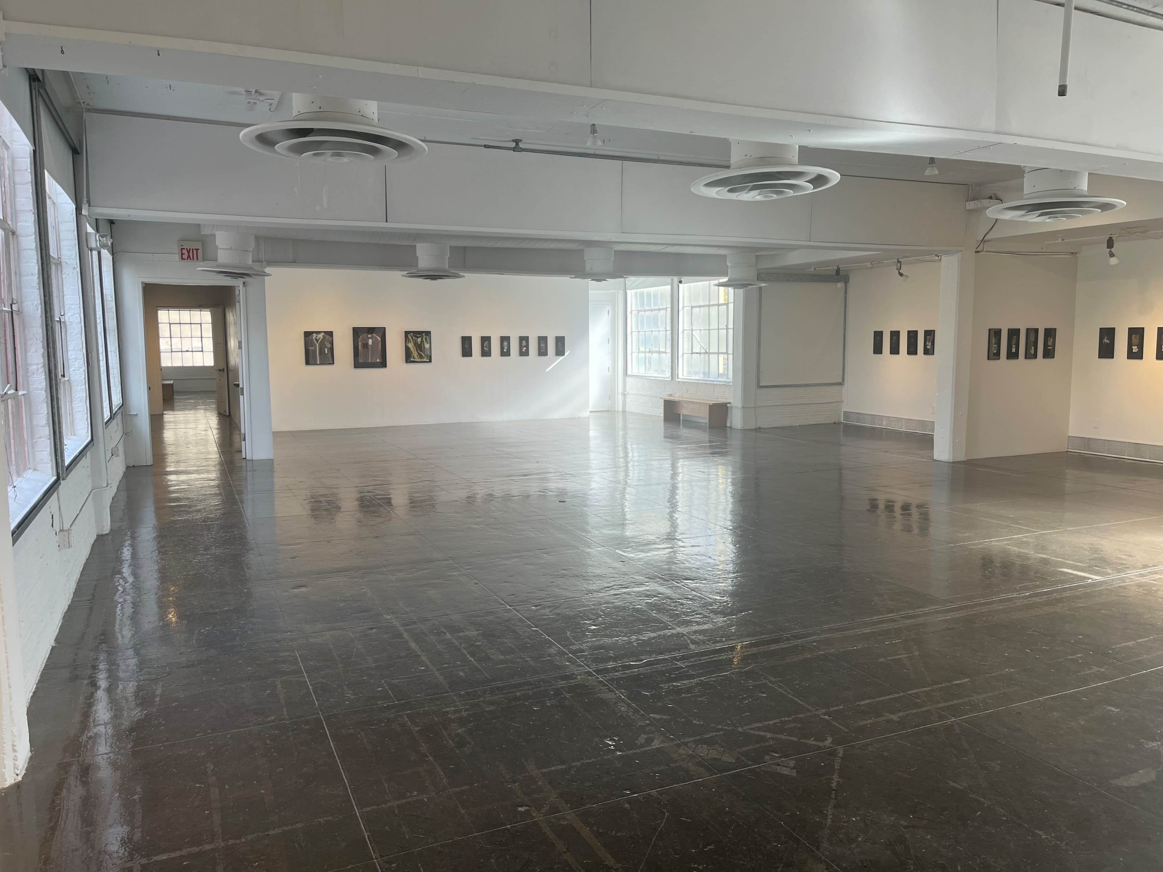 A spacious, brightly lit art gallery with polished floors and framed artworks displayed on the walls.
