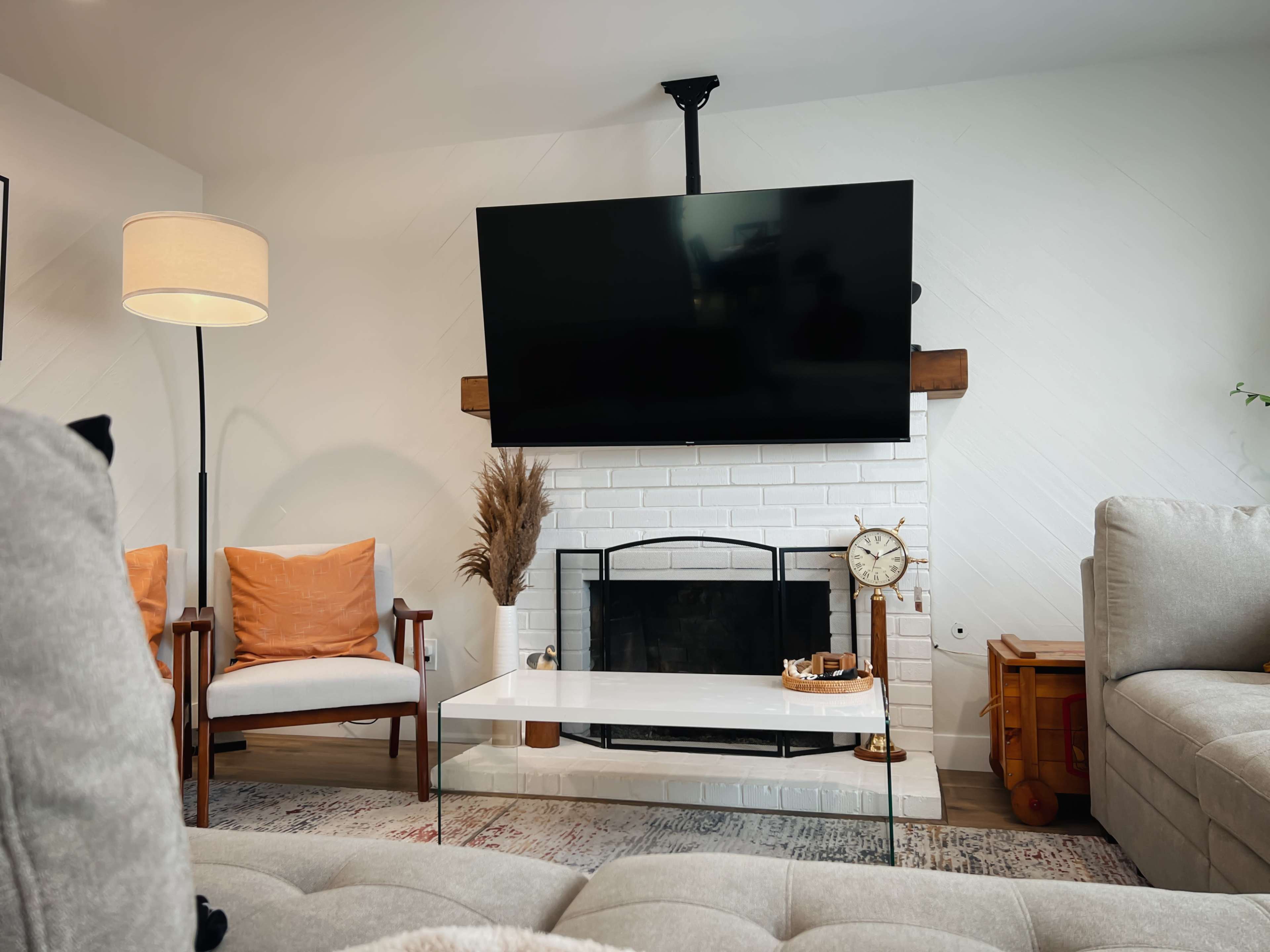 A modern living room with a mounted television above a white fireplace, flanked by two chairs and a coffee table in front.