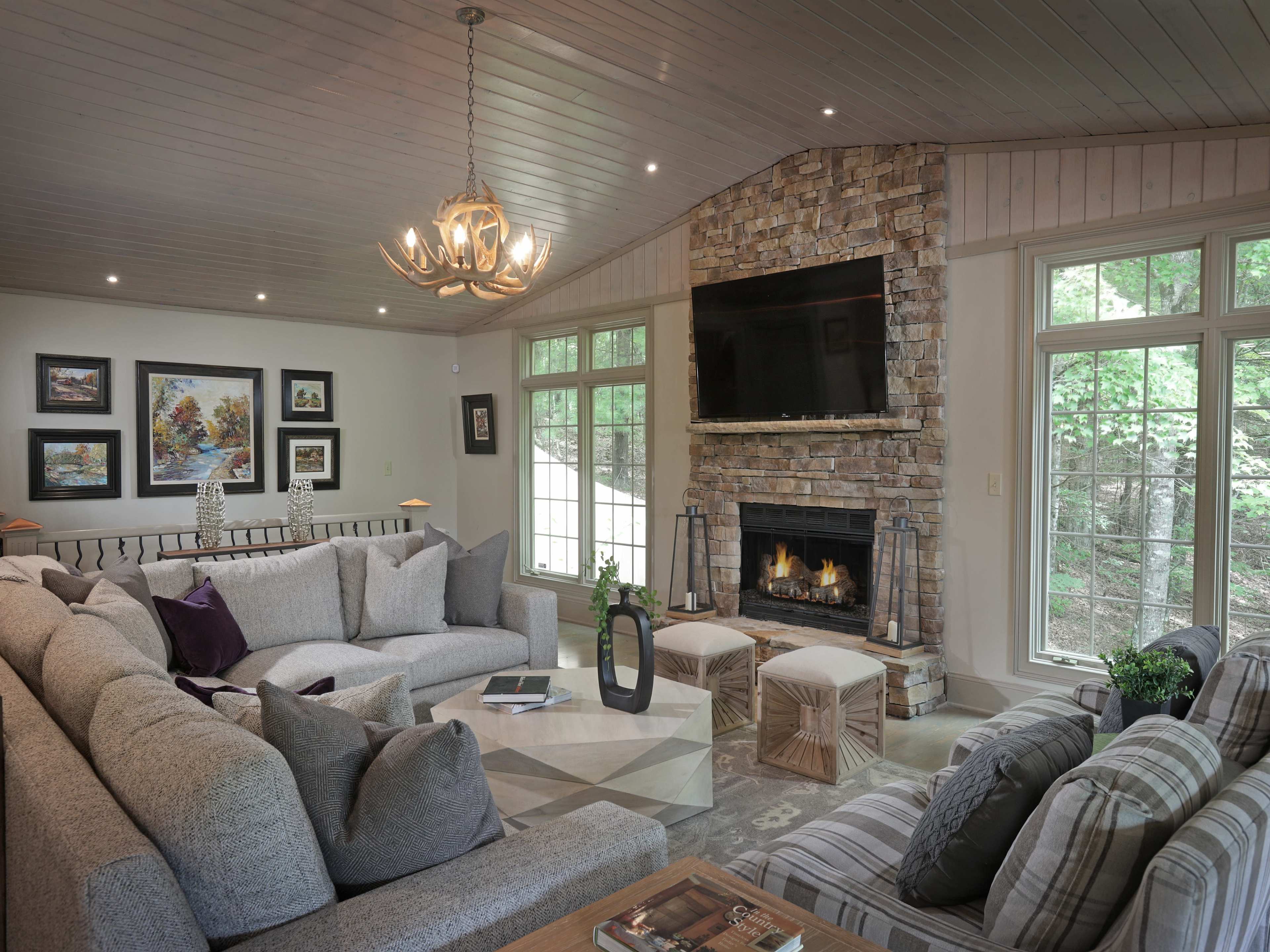 The living room features a large sectional sofa, a stone fireplace, and large windows allowing natural light to fill the space.