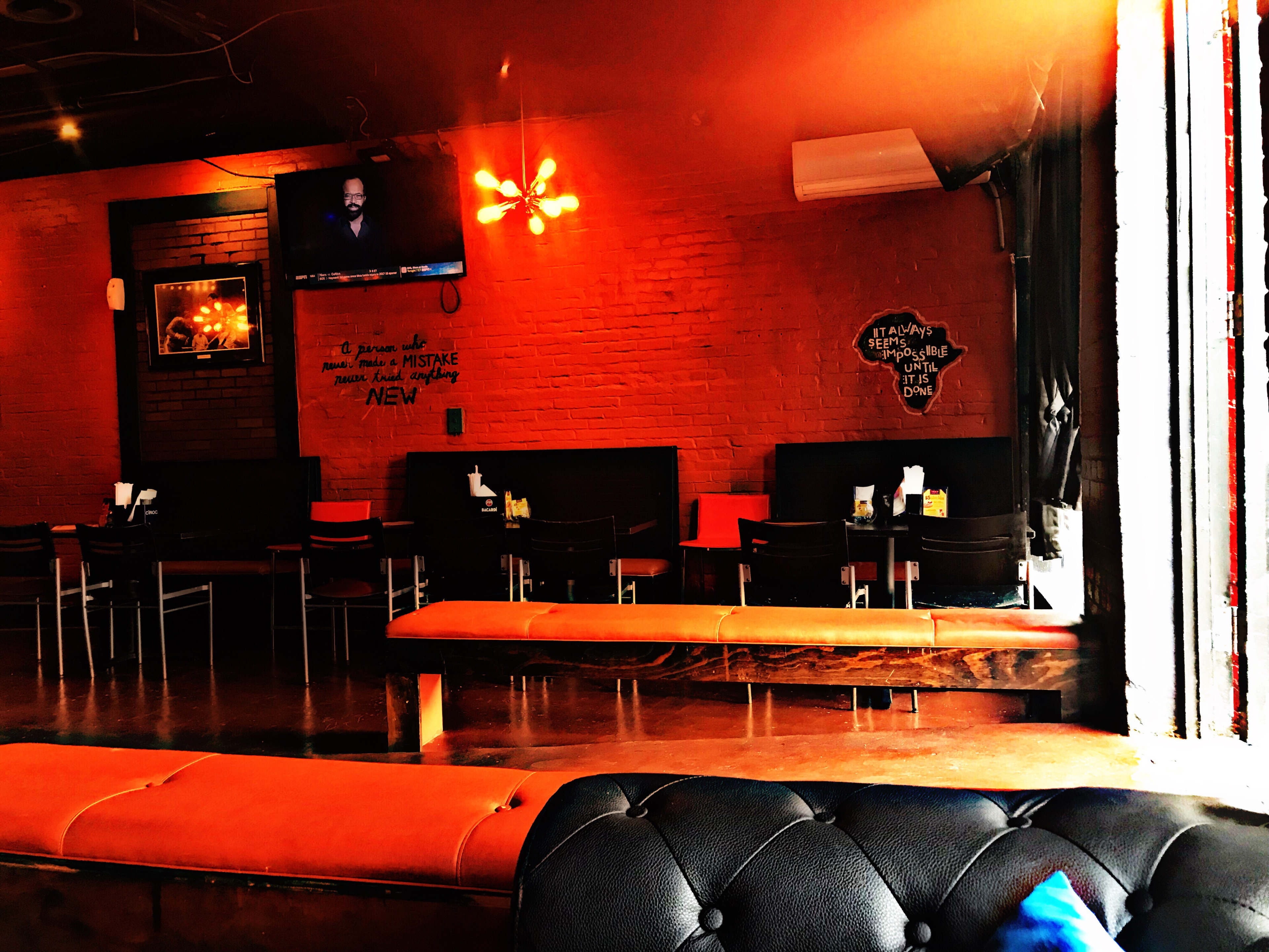 The image shows a restaurant interior with orange walls, black furniture, and a television mounted on the wall.