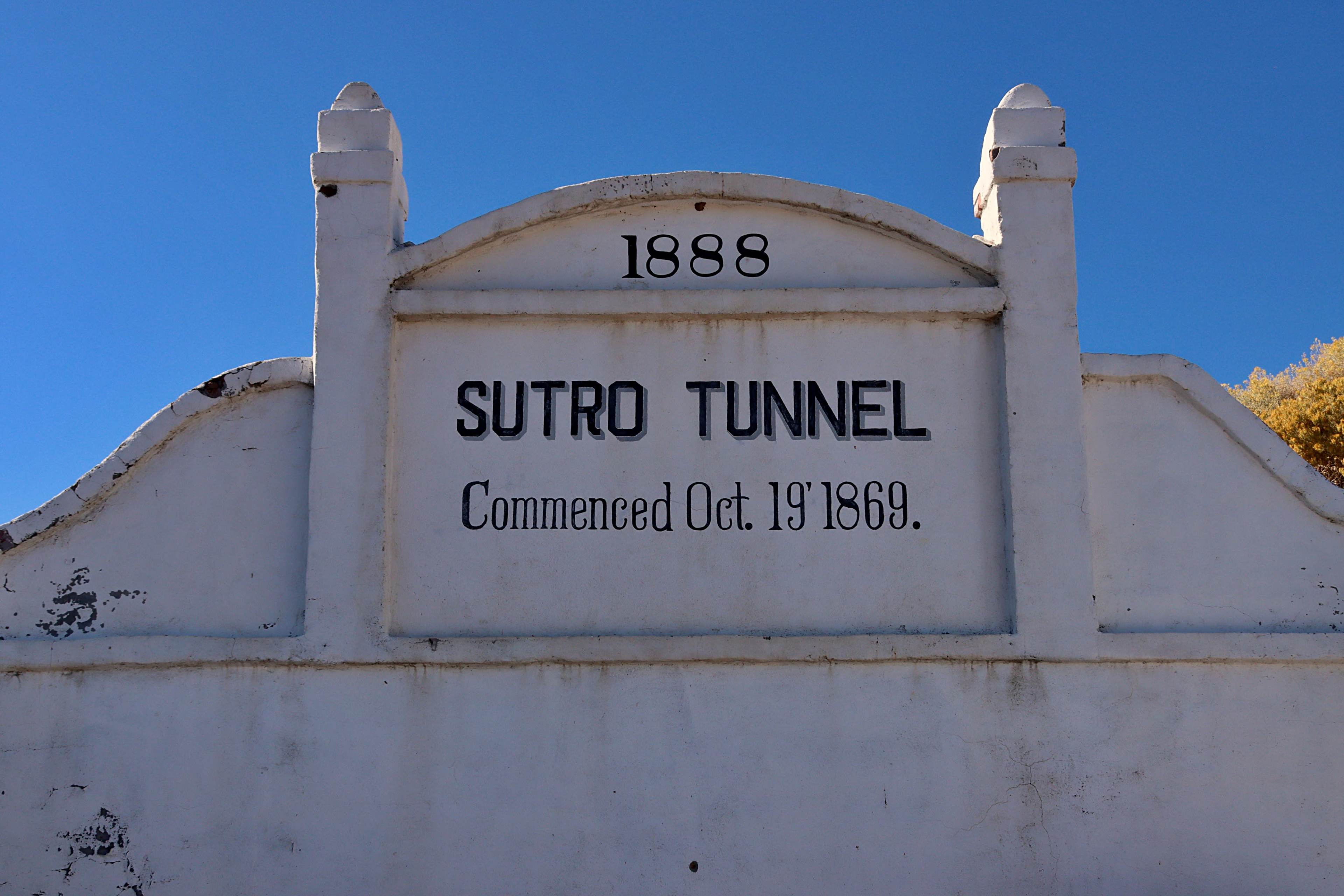 A white stone structure with a sign that reads "SUTRO TUNNEL" and the dates "Commenced Oct. 19, 1869" and "1888" prominently displayed.