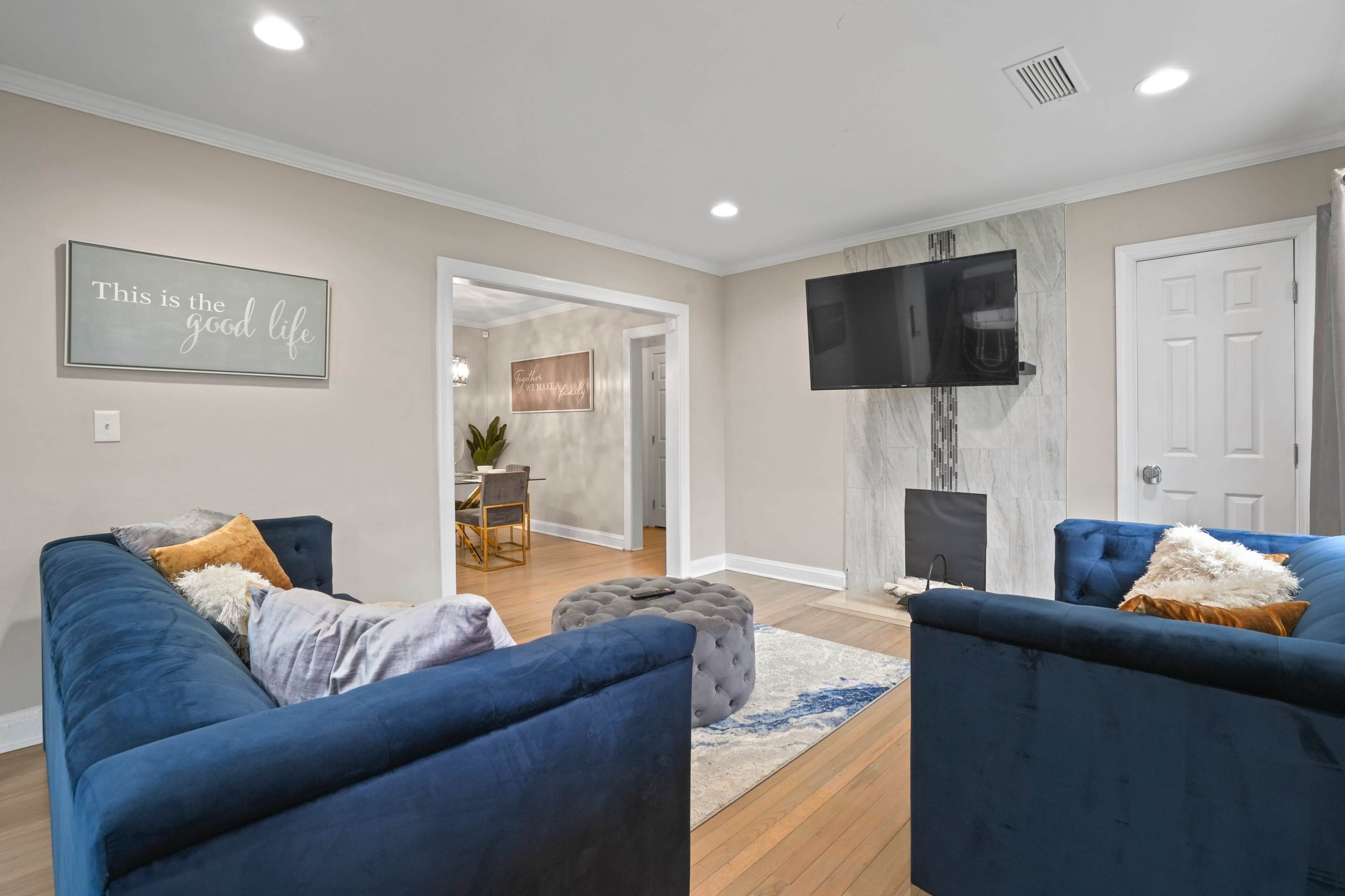 A modern living room features two blue sofas, a marble-accented wall with a mounted TV, and a view into an adjoining room with a dining area.