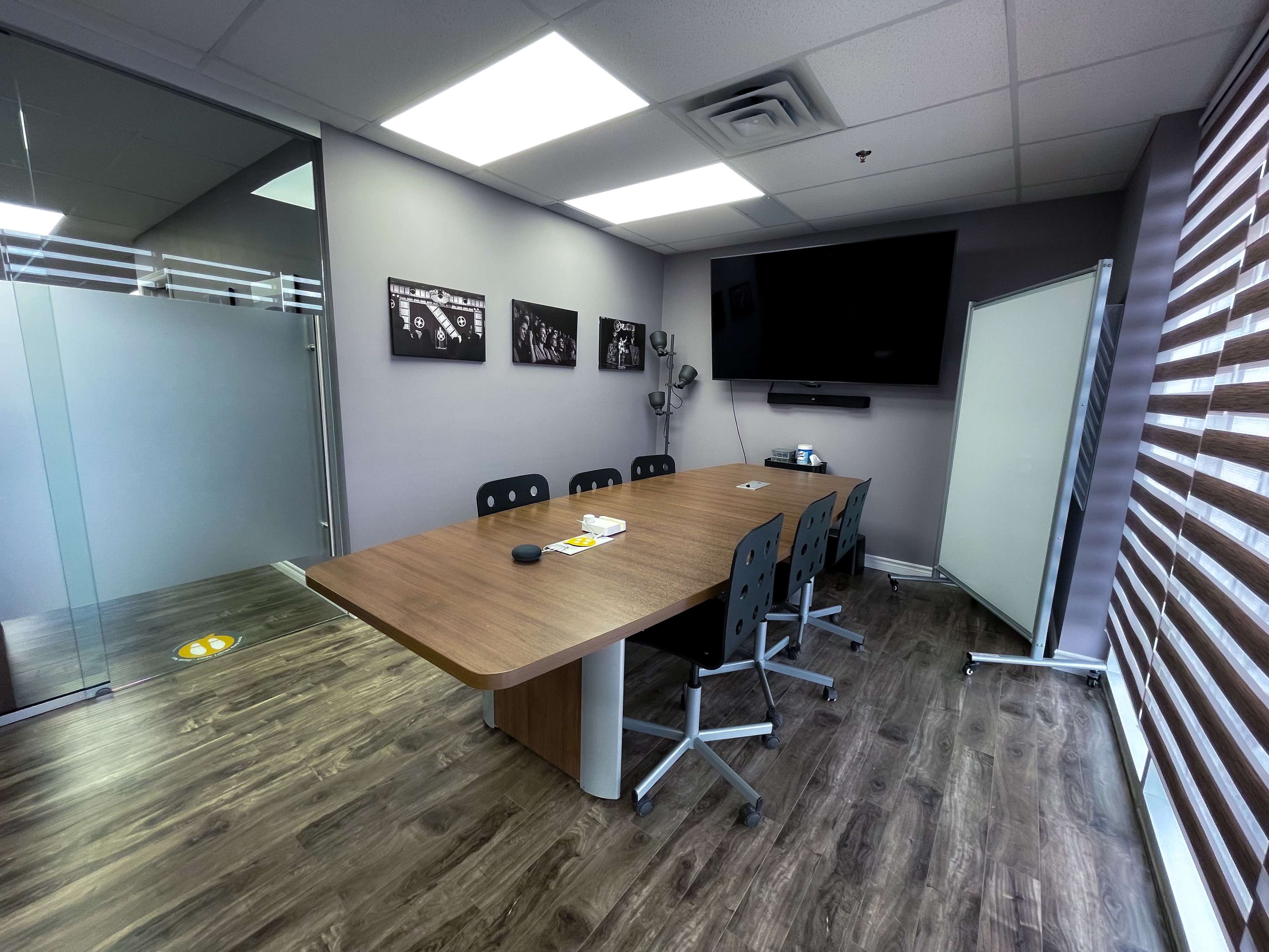 A modern conference room featuring a large wooden table surrounded by black chairs, a wall-mounted television, and a whiteboard.