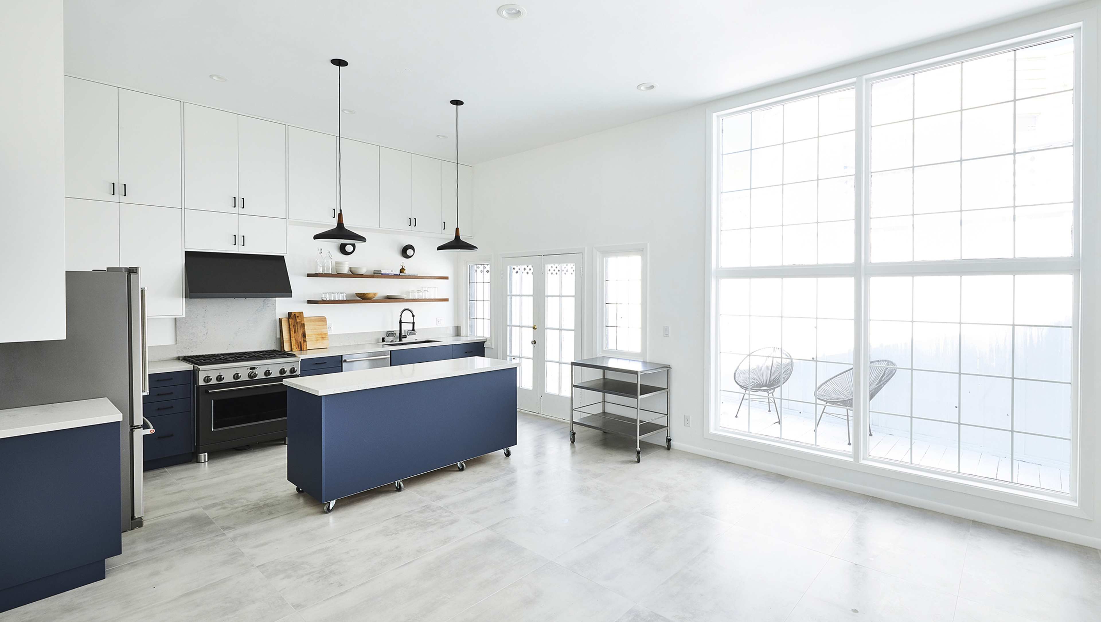 A modern kitchen with white cabinetry, a dark blue island, and large windows providing natural light.