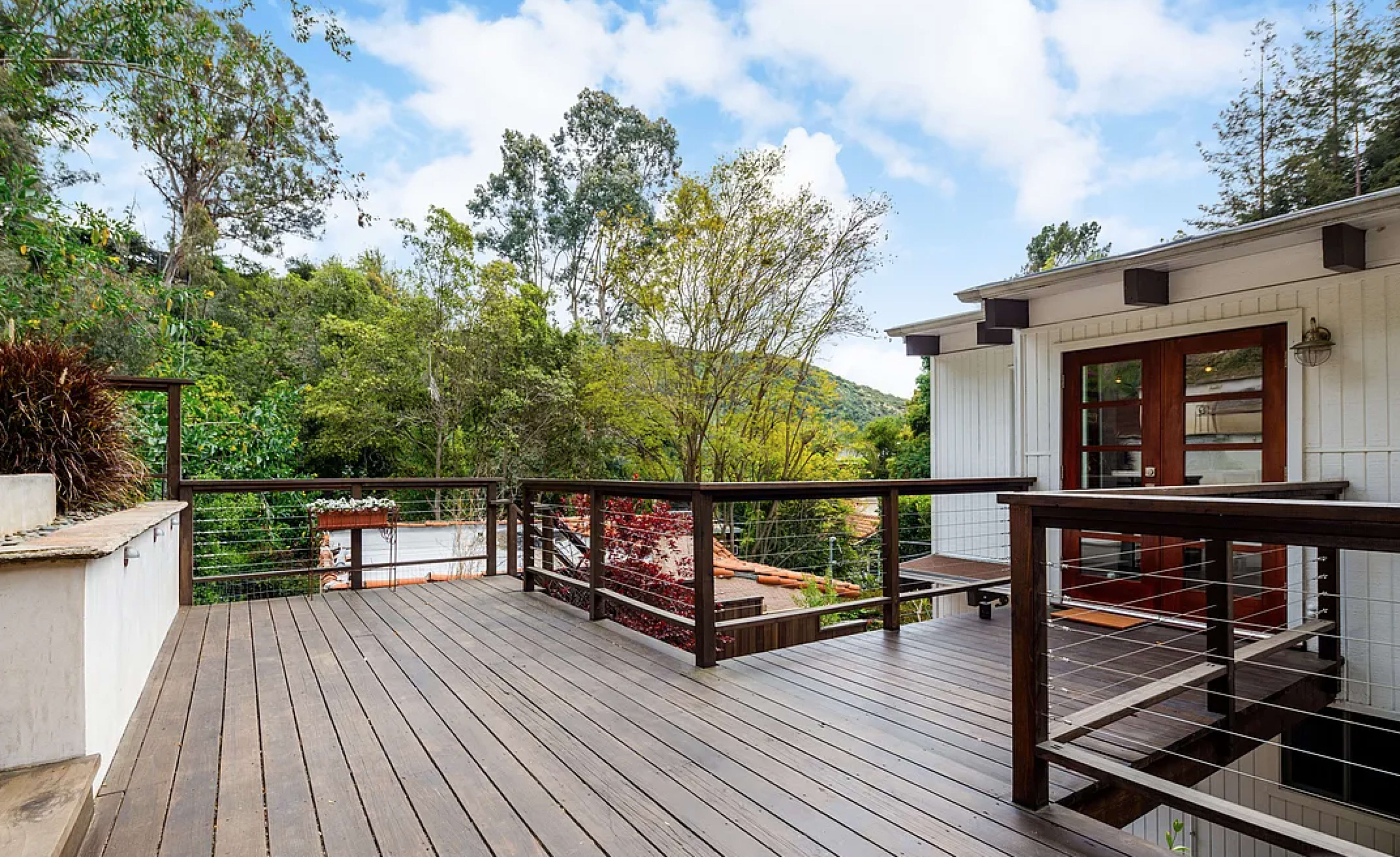 A wooden deck overlooks a lush green landscape with trees and a distant hill.