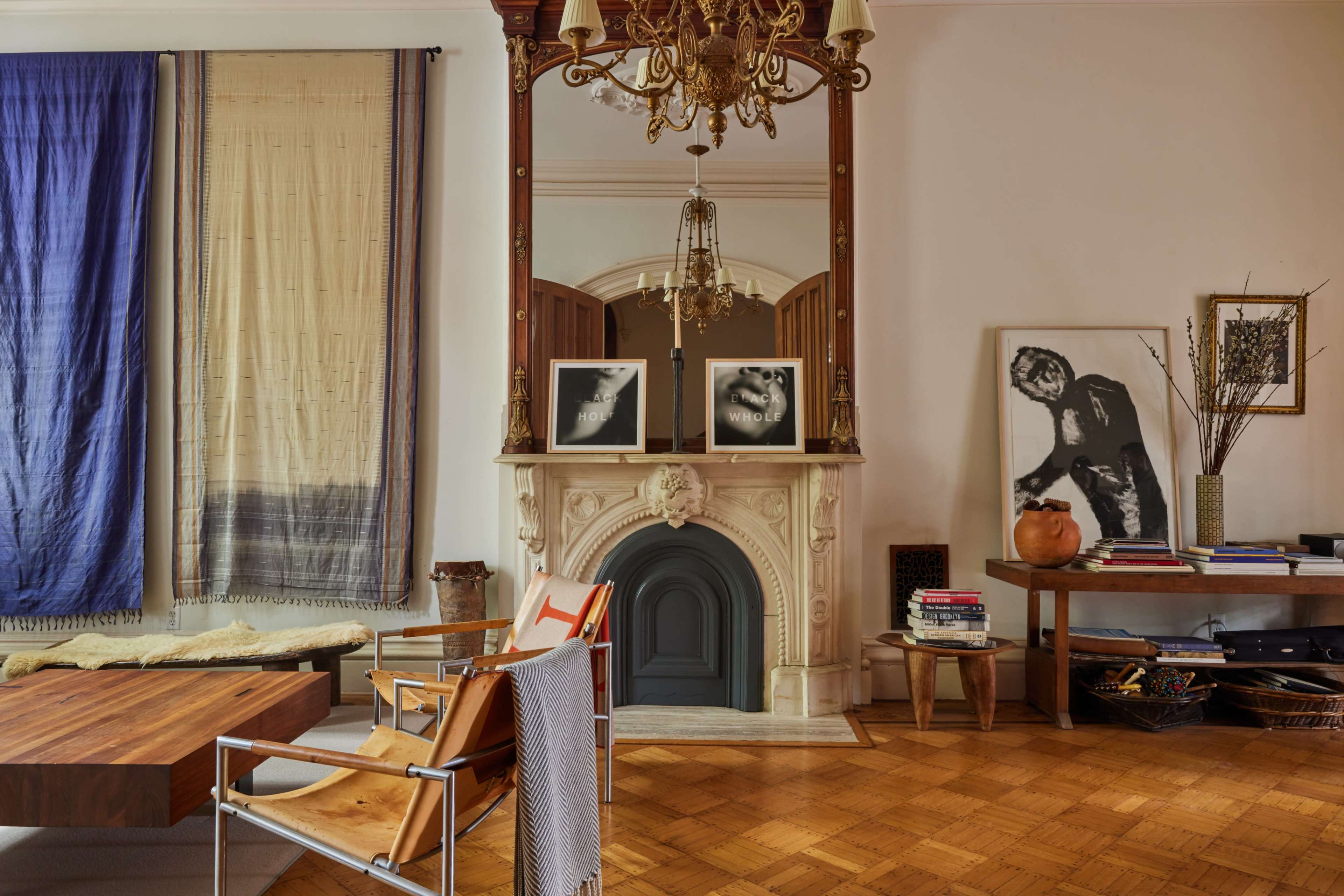 A stylish room featuring a fireplace with a large mirror above it, decorated with two framed pictures, alongside a wooden table and a chair.