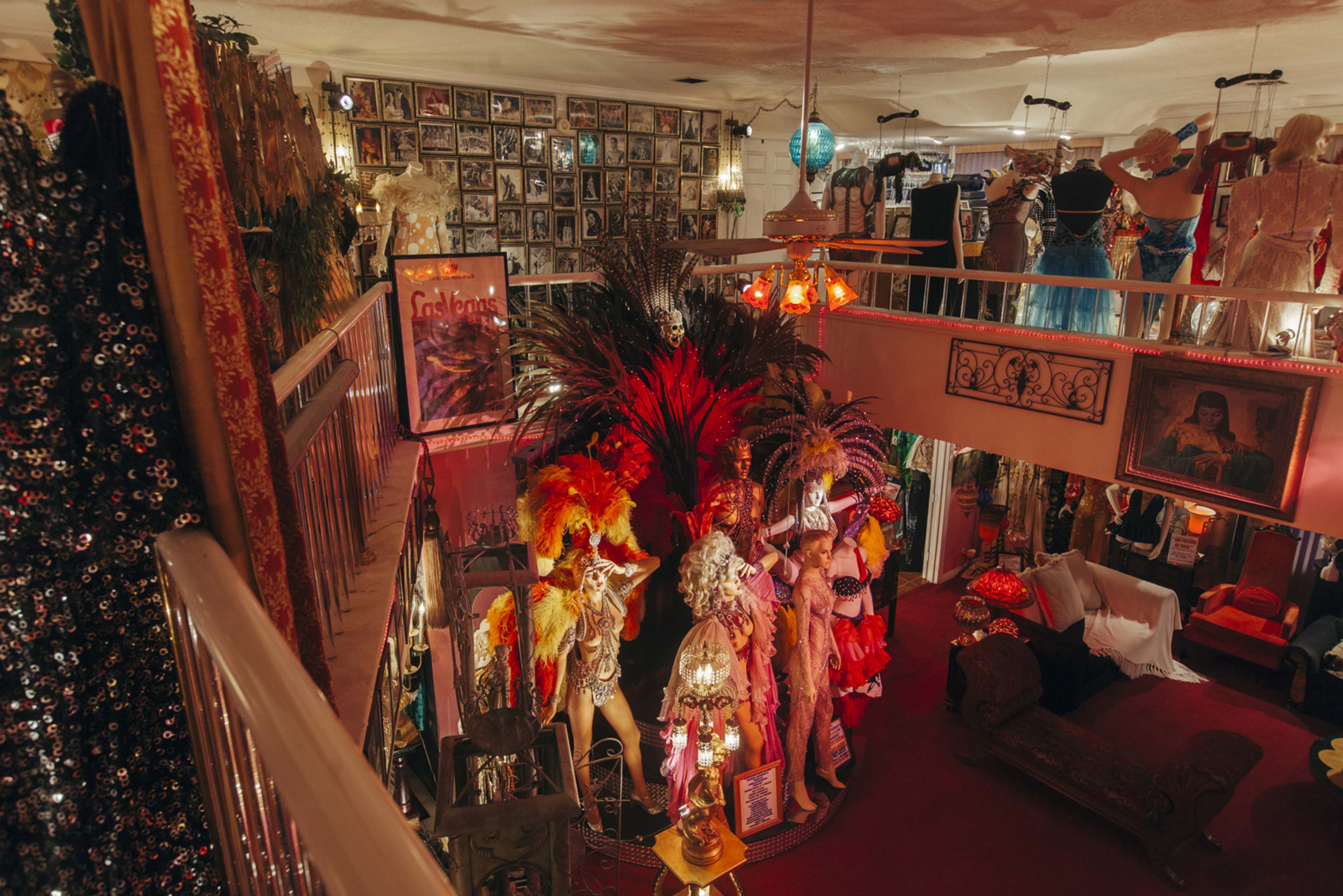 The image depicts an eclectic vintage costume shop filled with colorful costumes, photographs on the walls, and decorative items arranged around a central display area.
