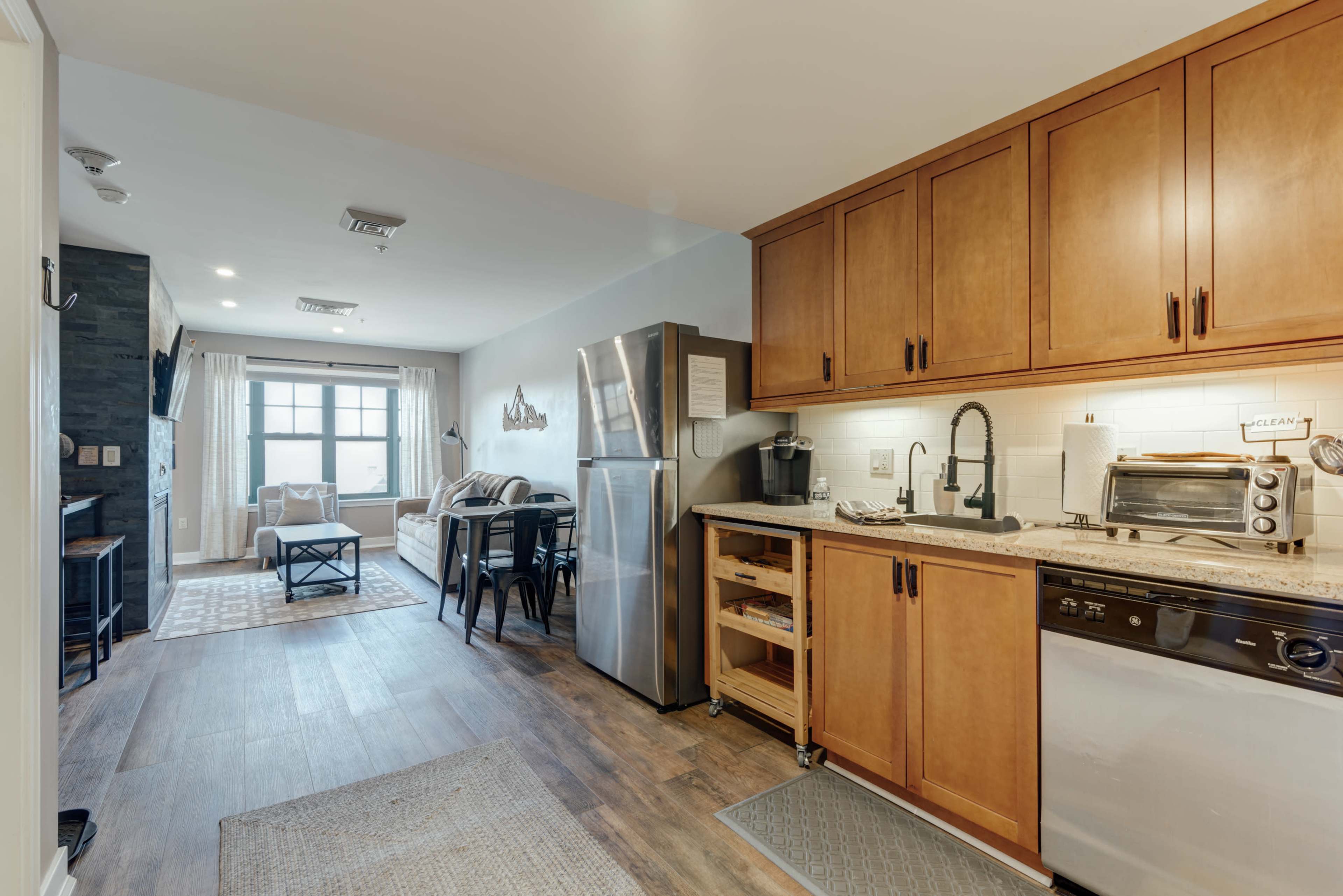 A modern kitchen with wooden cabinets and stainless steel appliances, adjacent to a dining area featuring a table and chairs.